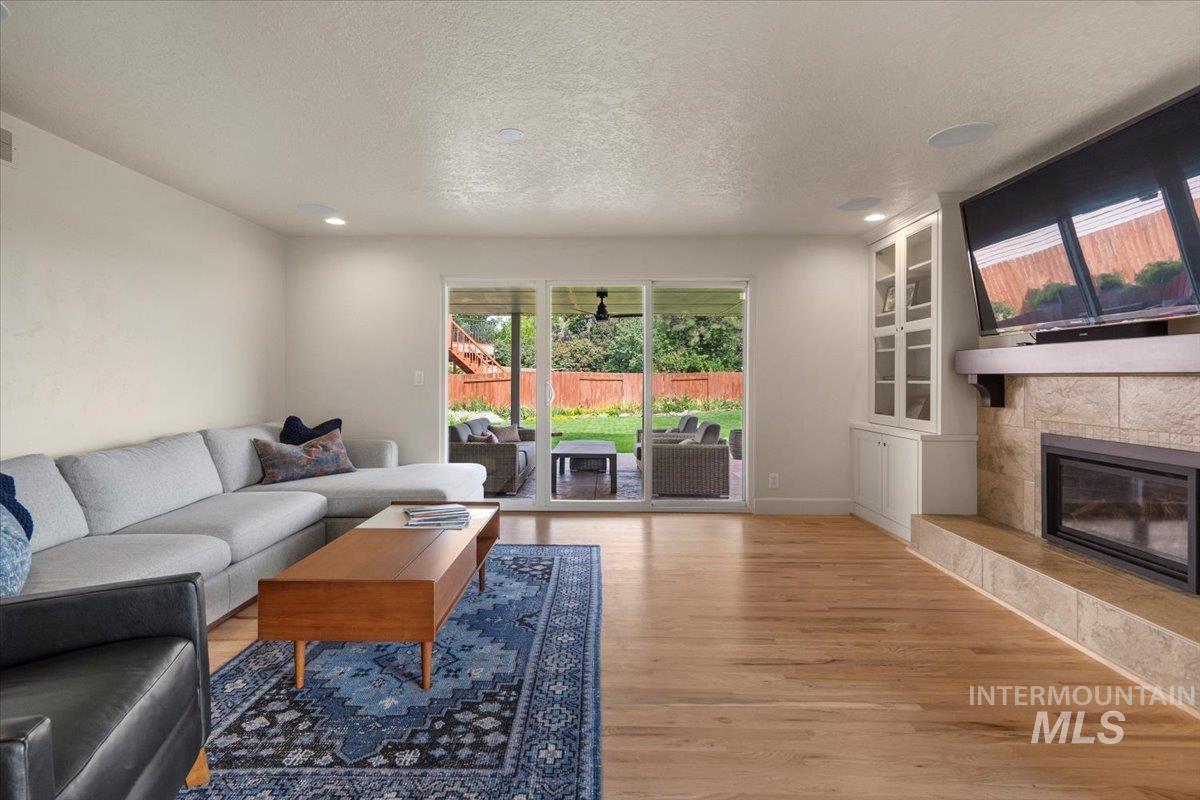 Living area with light wood-type flooring, a tile fireplace, a textured ceiling, built in shelves, and recessed lighting