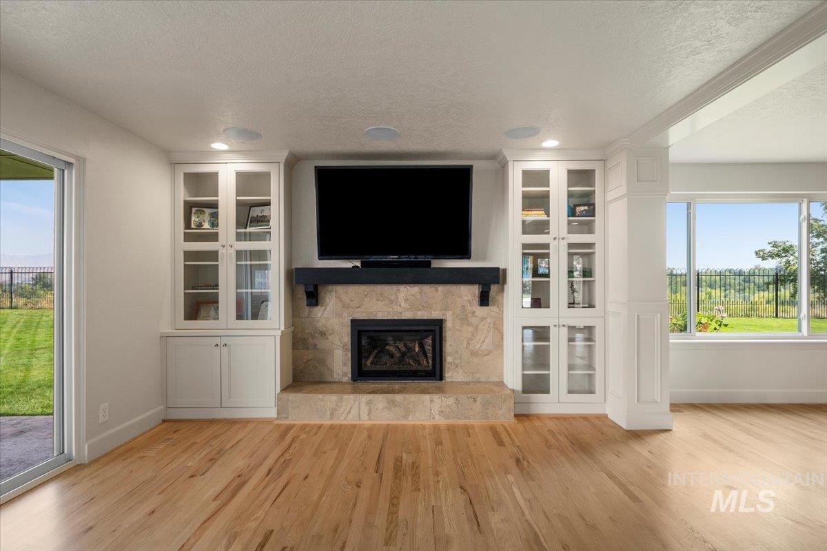 Unfurnished living room with a glass covered fireplace, light wood-type flooring, and a textured ceiling