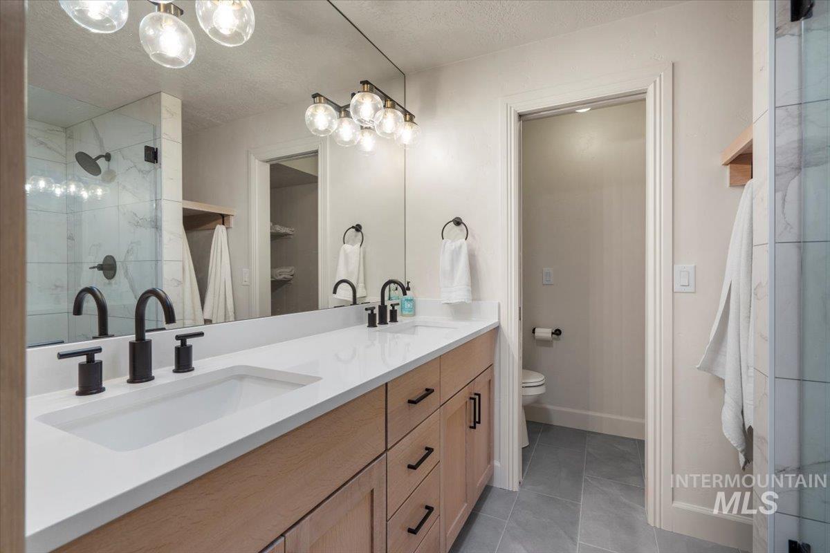Full bath featuring double vanity, a textured ceiling, light tile patterned floors, and a tile shower