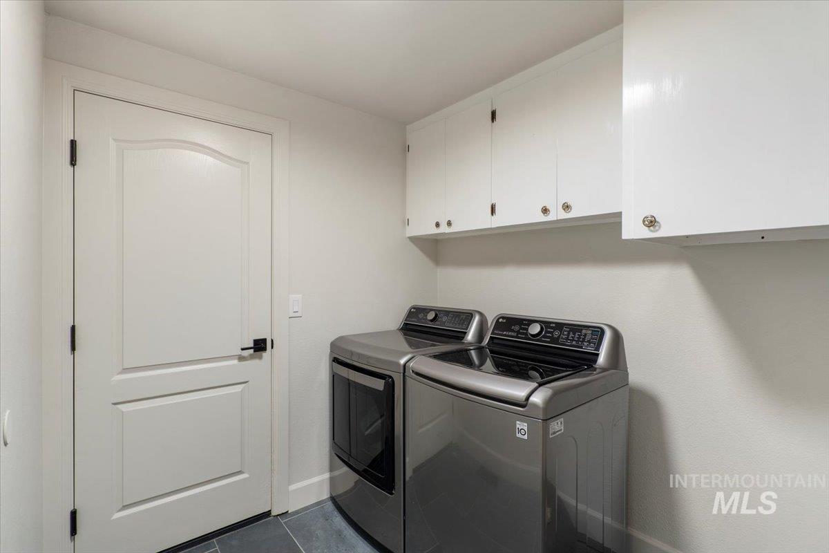 Washroom featuring cabinet space, separate washer and dryer, and dark tile patterned flooring