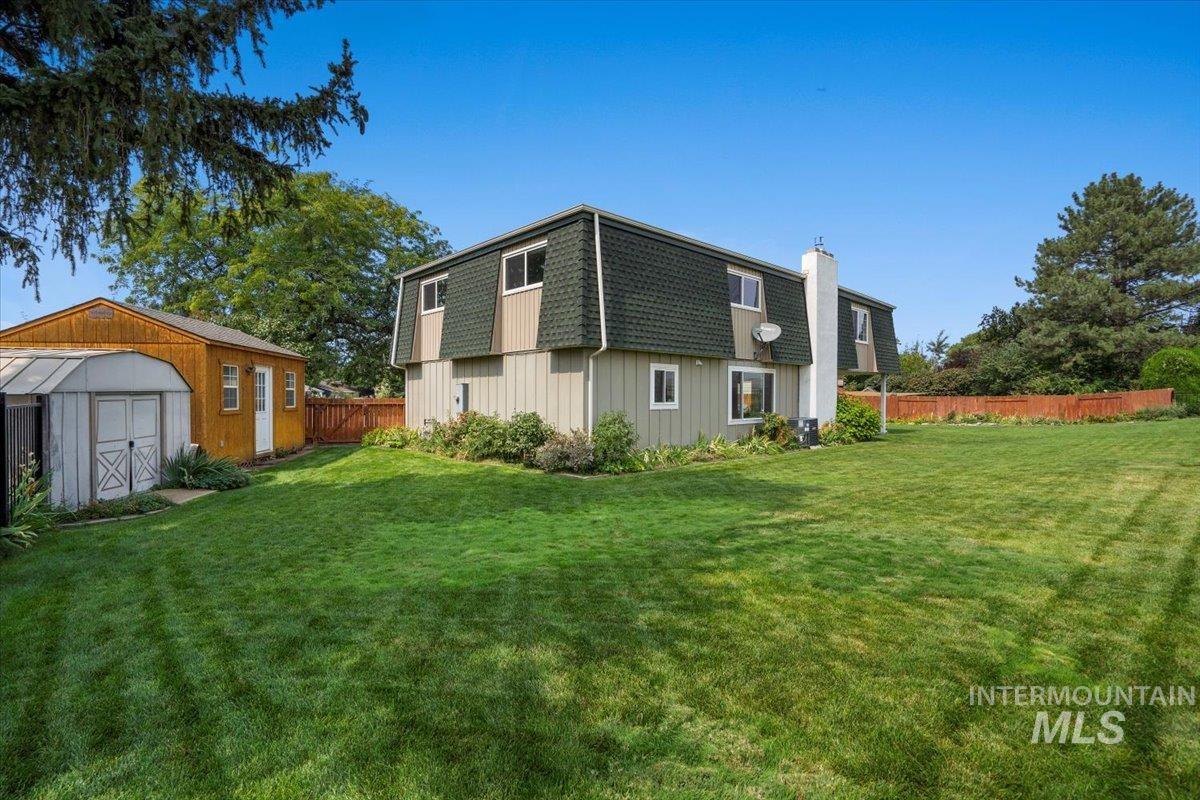 Rear view of property featuring a storage unit, mansard roof, and roof with shingles