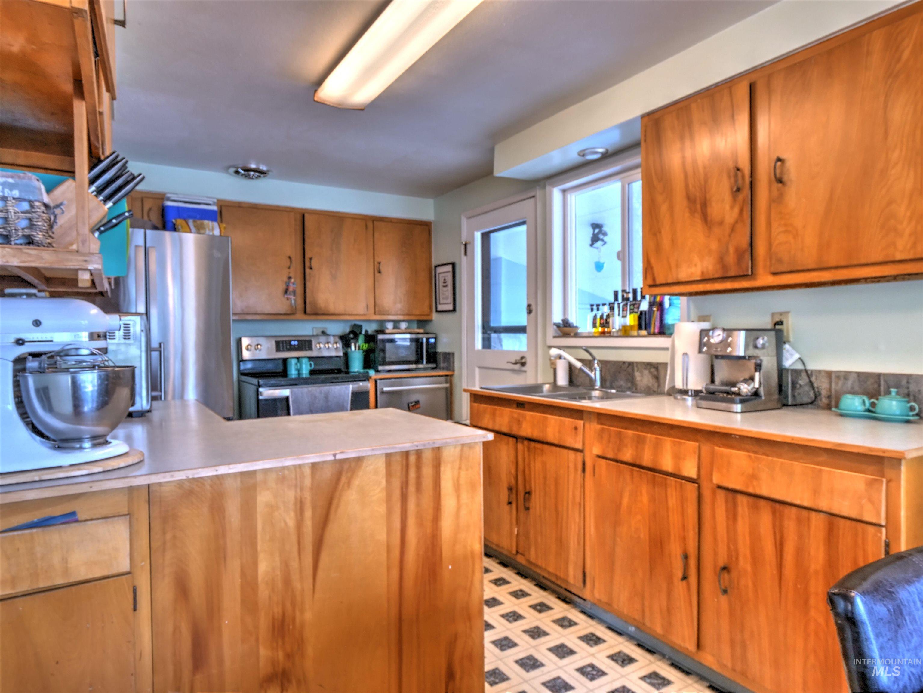 Kitchen featuring brown cabinetry, light countertops, appliances with stainless steel finishes, a peninsula, and light floors