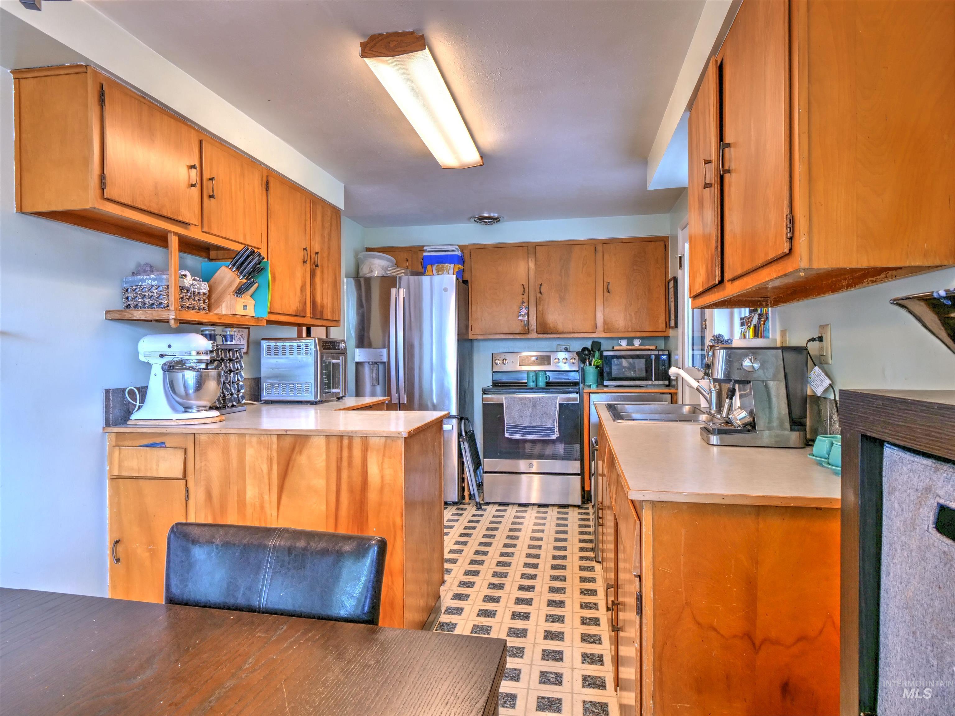 Kitchen with brown cabinetry, appliances with stainless steel finishes, light countertops, a peninsula, and light flooring
