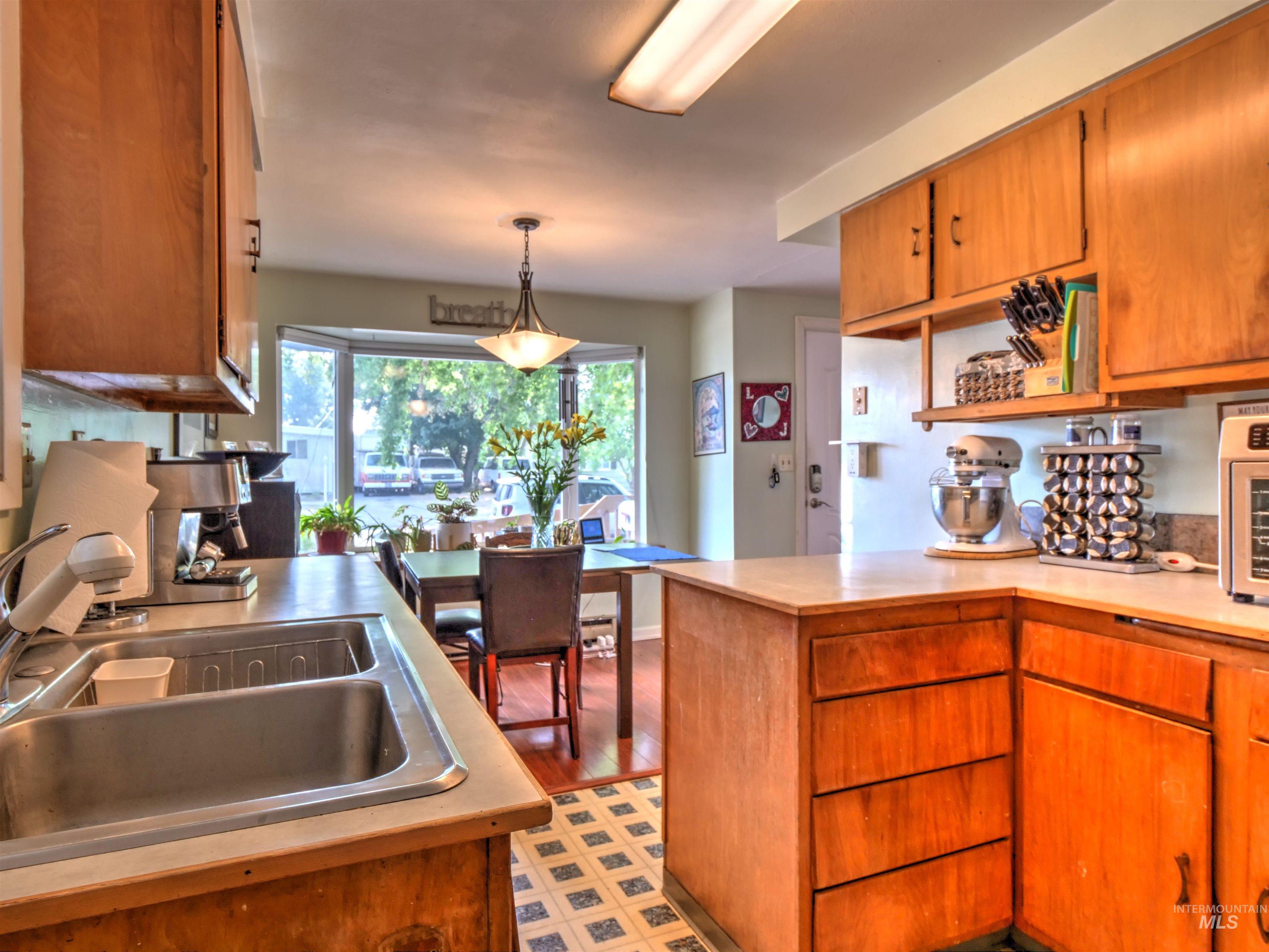 Kitchen with brown cabinetry, light countertops, decorative light fixtures, open shelves, and light wood-type flooring