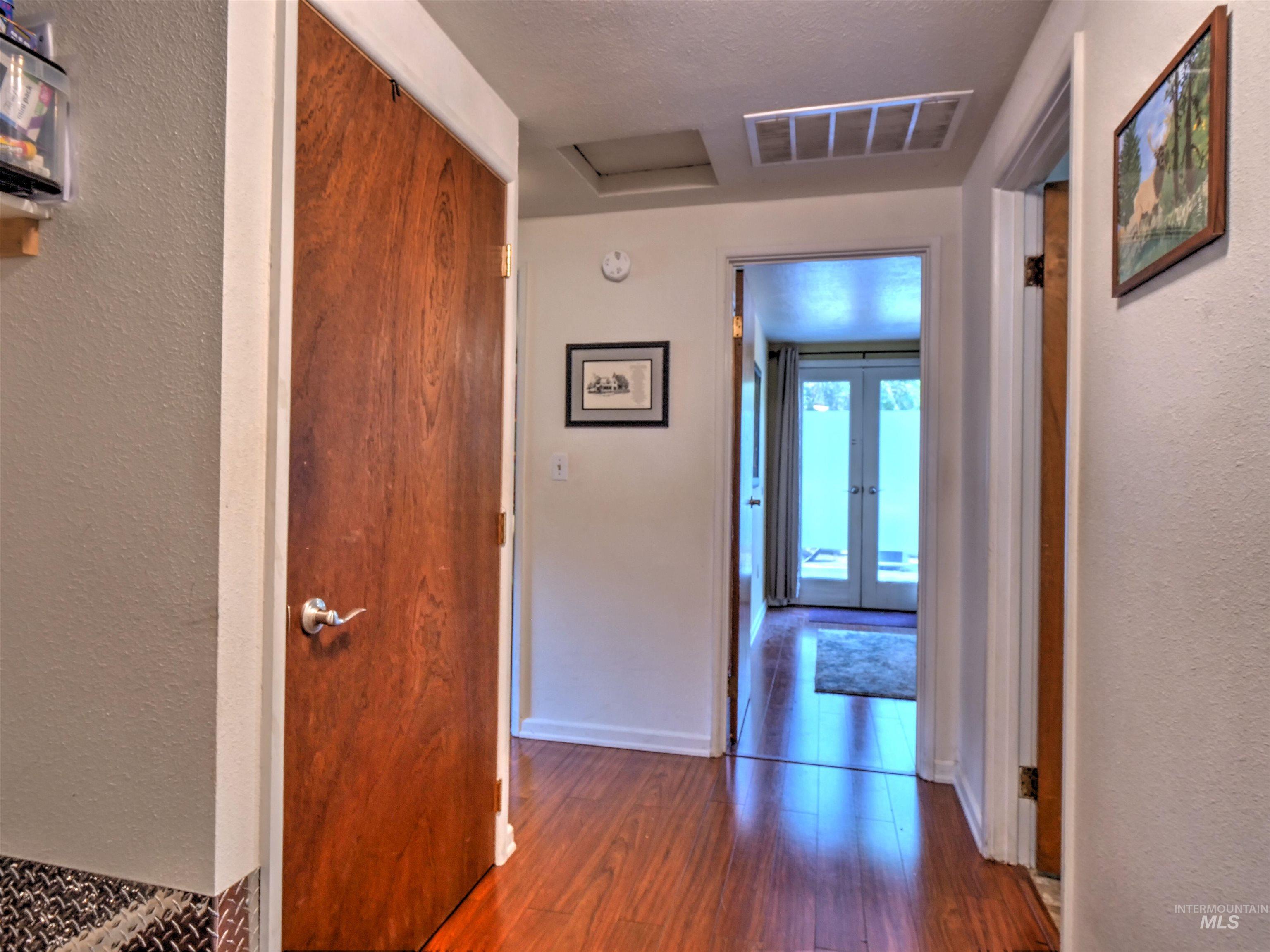 Hall featuring a textured wall, dark wood-style floors, attic access, and french doors