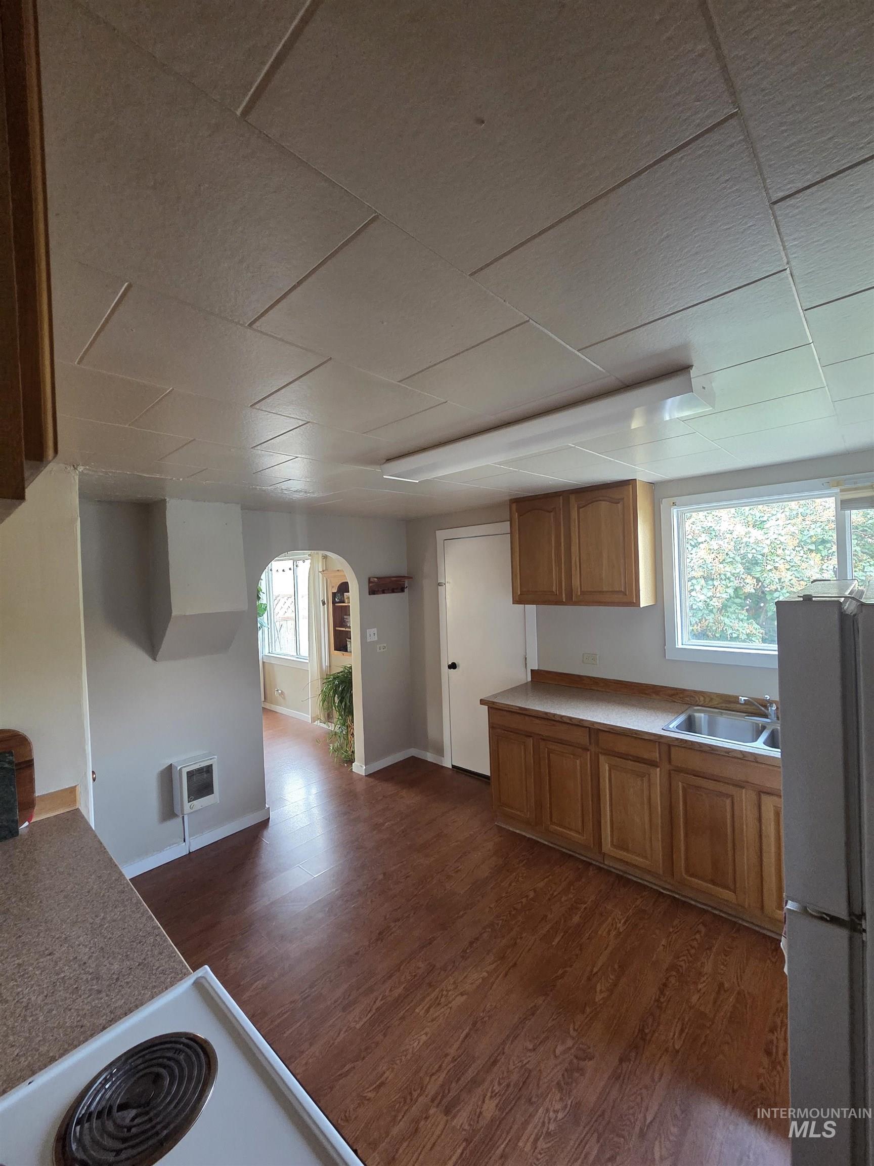Kitchen featuring arched walkways, freestanding refrigerator, dark wood-style flooring, and healthy amount of natural light