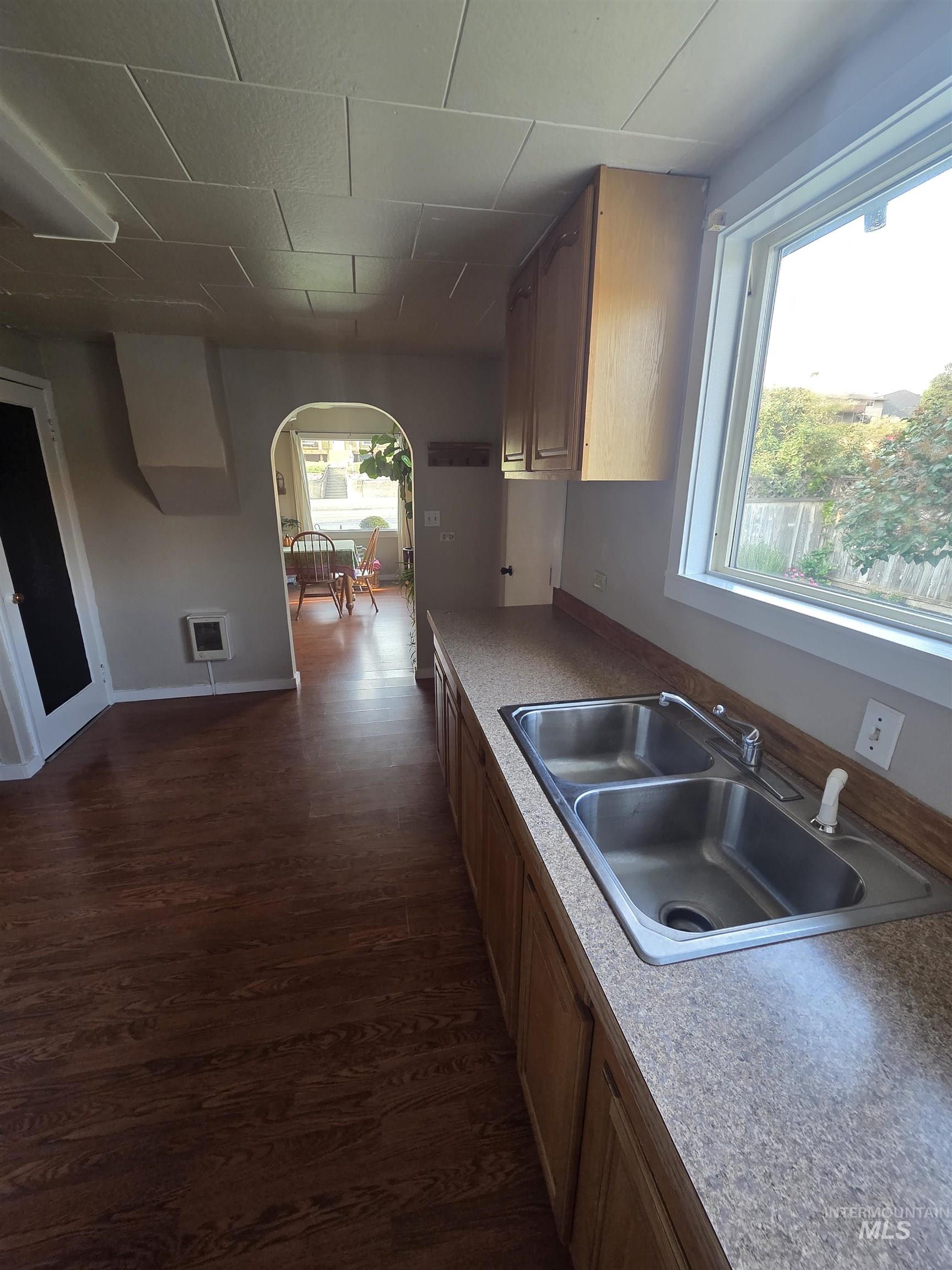 Kitchen featuring arched walkways, dark wood-style flooring, light countertops, and brown cabinets