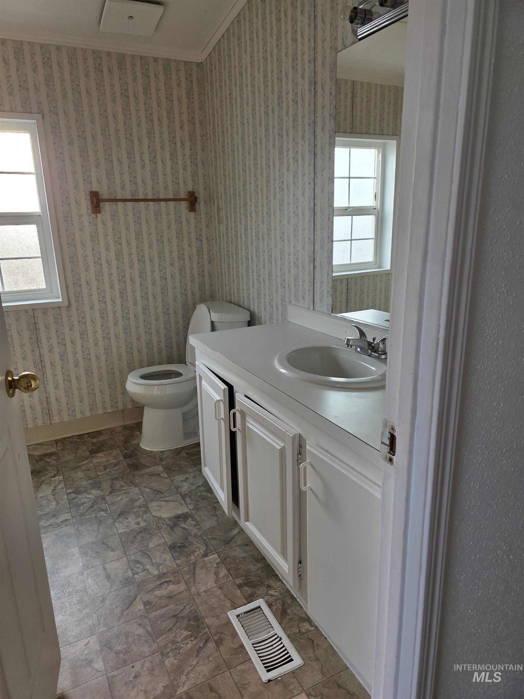 Bathroom featuring vanity, ornamental molding, and wallpapered walls