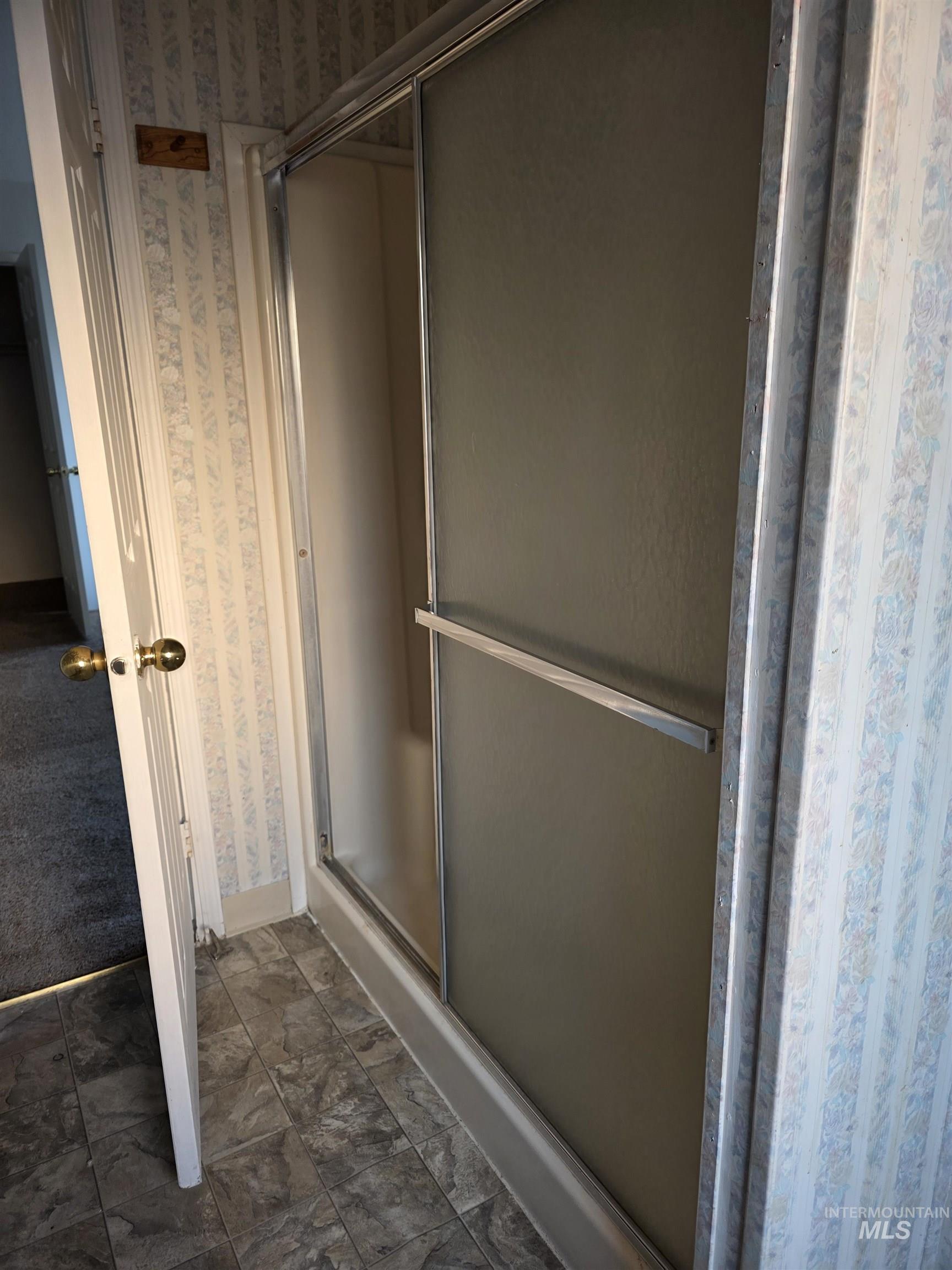 Full bathroom featuring wallpapered walls and a shower stall