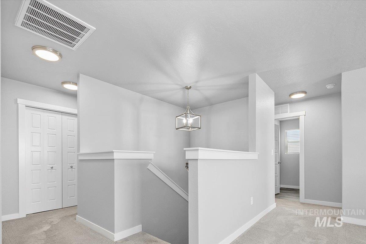 Corridor with an upstairs landing, light carpet, a chandelier, and a textured ceiling