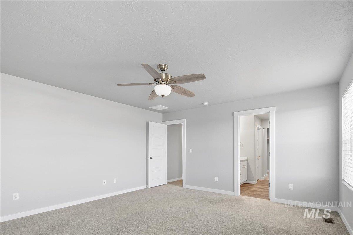 Unfurnished bedroom with light carpet, a textured ceiling, ceiling fan, and connected bathroom
