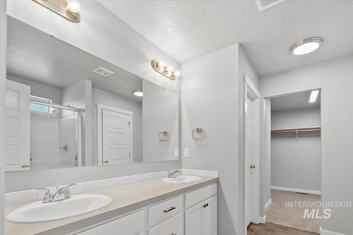 Full bath with a shower stall, double vanity, a spacious closet, wood finished floors, and a textured ceiling