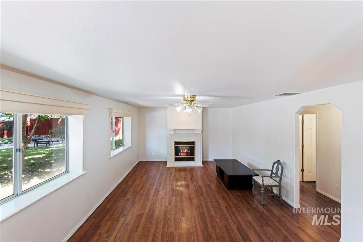 Unfurnished living room with dark wood-style floors, a ceiling fan, arched walkways, and a tile fireplace