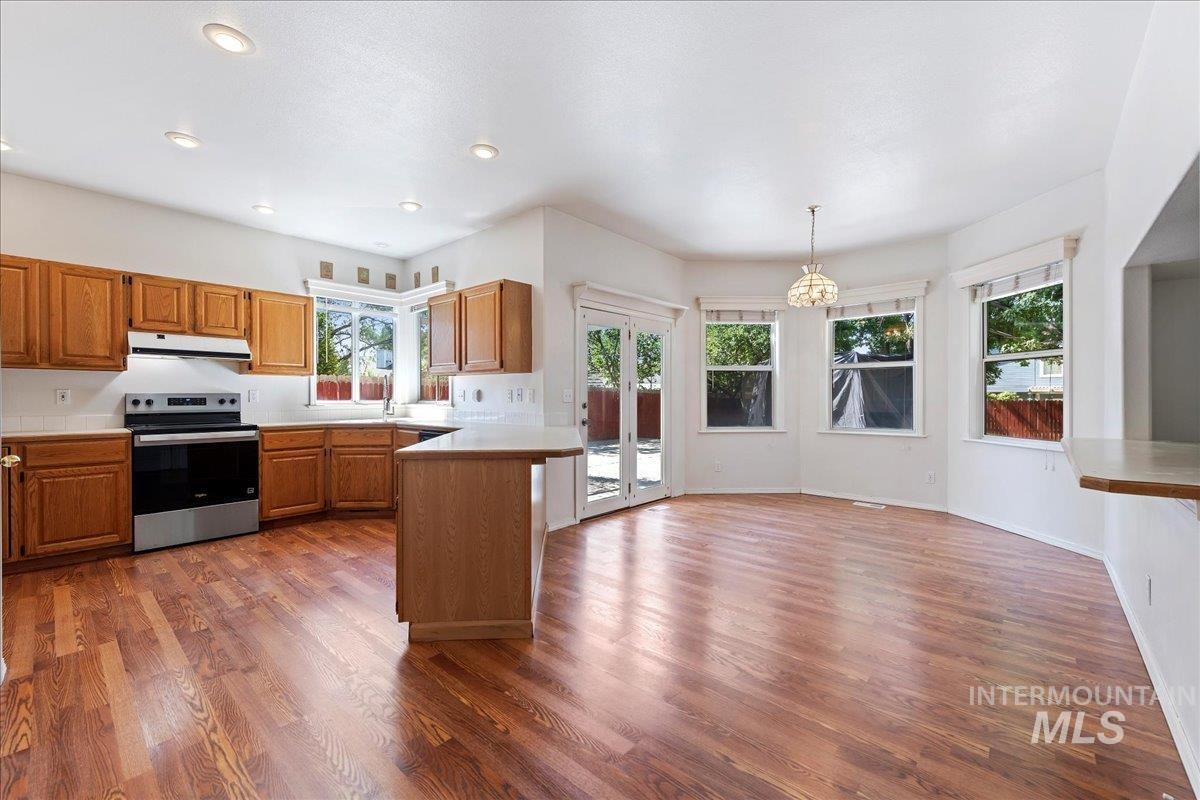 Kitchen featuring electric range, brown cabinets, dark wood-type flooring, a peninsula, and light countertops