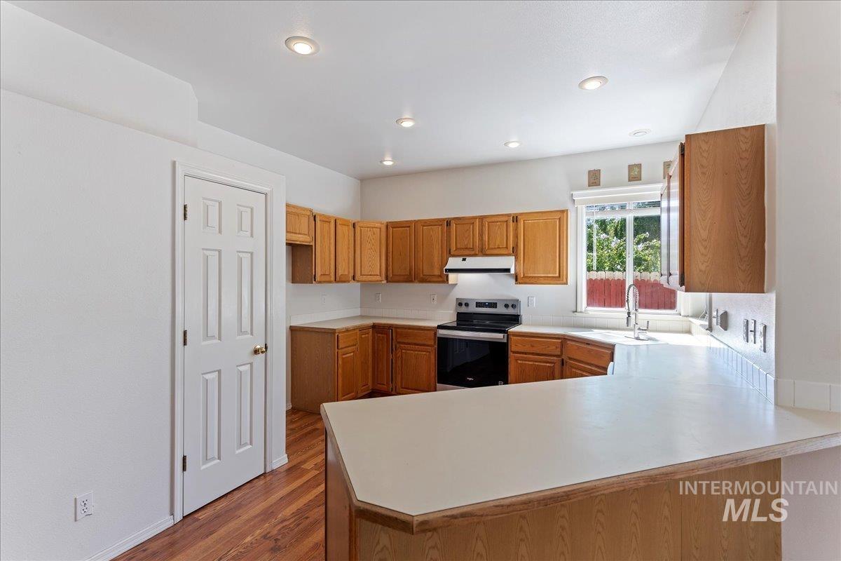 Kitchen featuring light countertops, a peninsula, electric stove, brown cabinetry, and dark wood-style floors