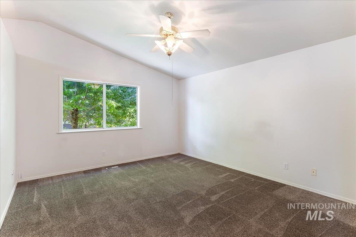 Spare room featuring lofted ceiling, dark carpet, and ceiling fan