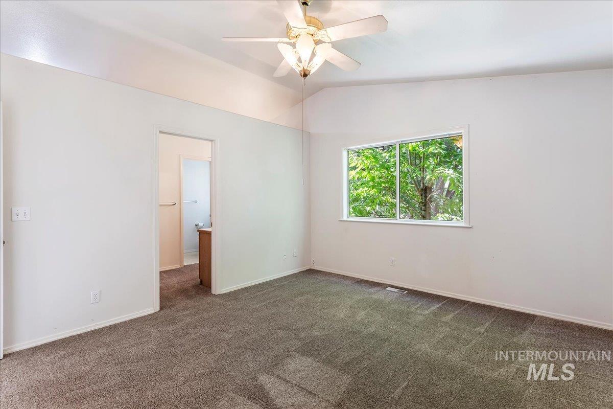 Unfurnished bedroom featuring dark colored carpet, lofted ceiling, ceiling fan, and ensuite bath