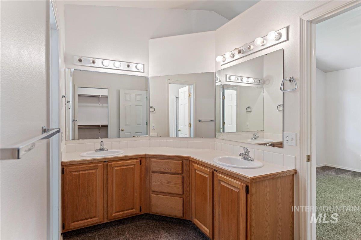 Full bath with double vanity, a spacious closet, and dark carpet