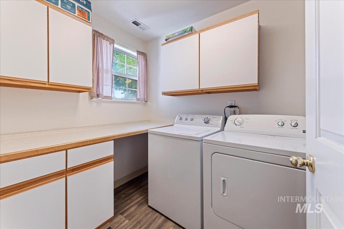 Washroom with dark wood-style flooring, cabinet space, and washing machine and dryer