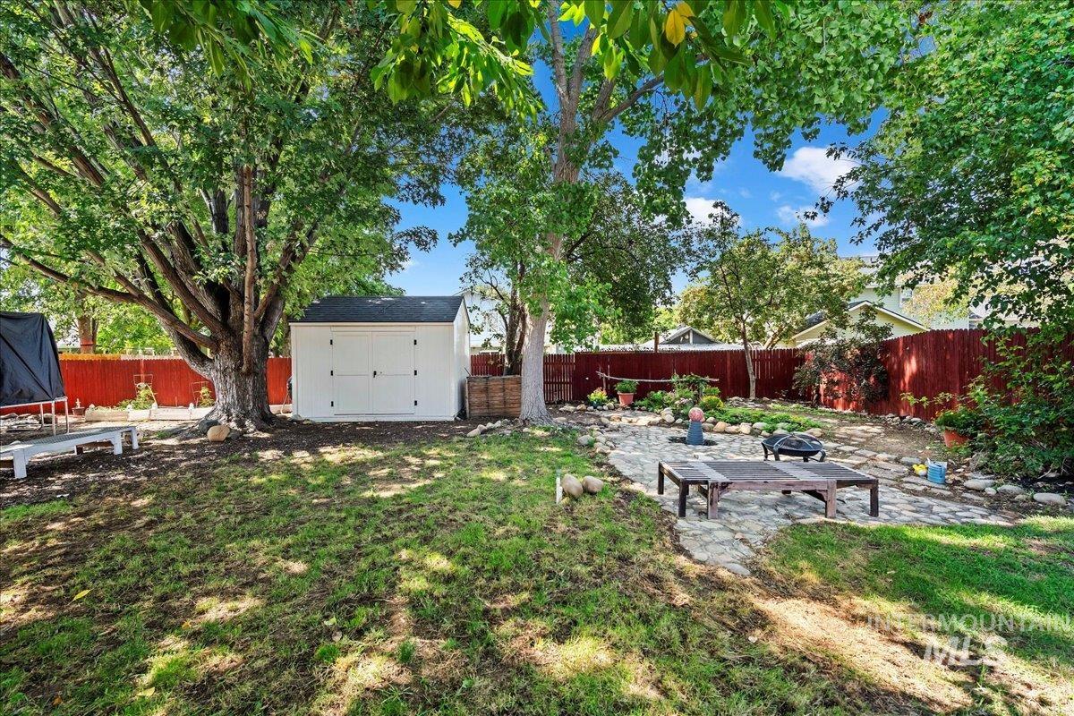 Fenced backyard featuring a patio area, a shed, and a fire pit