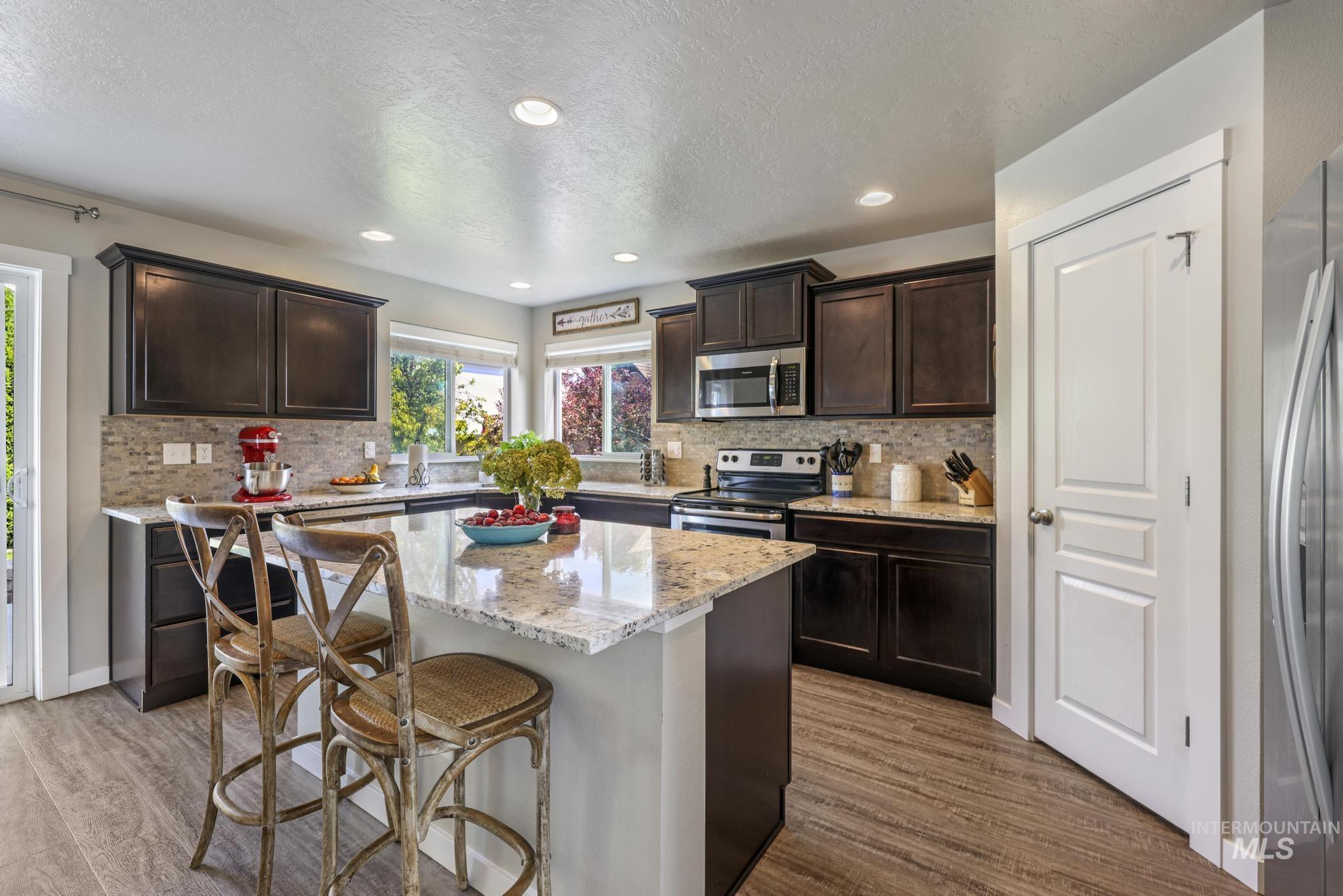 Kitchen featuring dark brown cabinetry, stainless steel appliances, a breakfast bar, light stone countertops, and recessed lighting