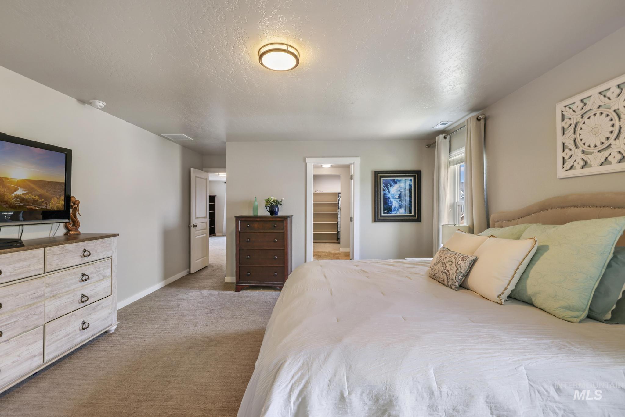 Bedroom with a spacious closet, a textured ceiling, and light colored carpet