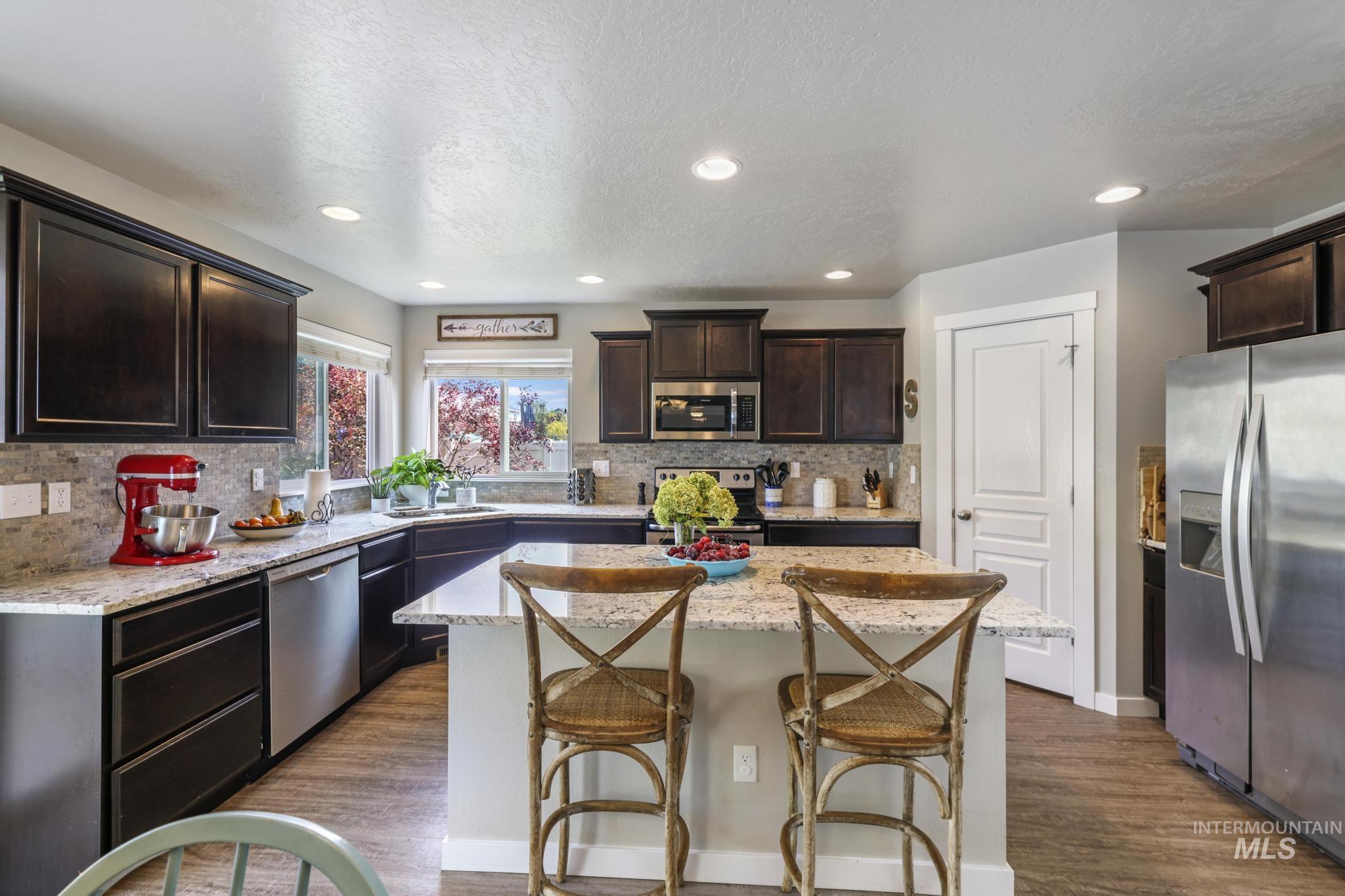 Kitchen featuring appliances with stainless steel finishes, dark brown cabinets, a kitchen island, a breakfast bar, and dark wood-style flooring