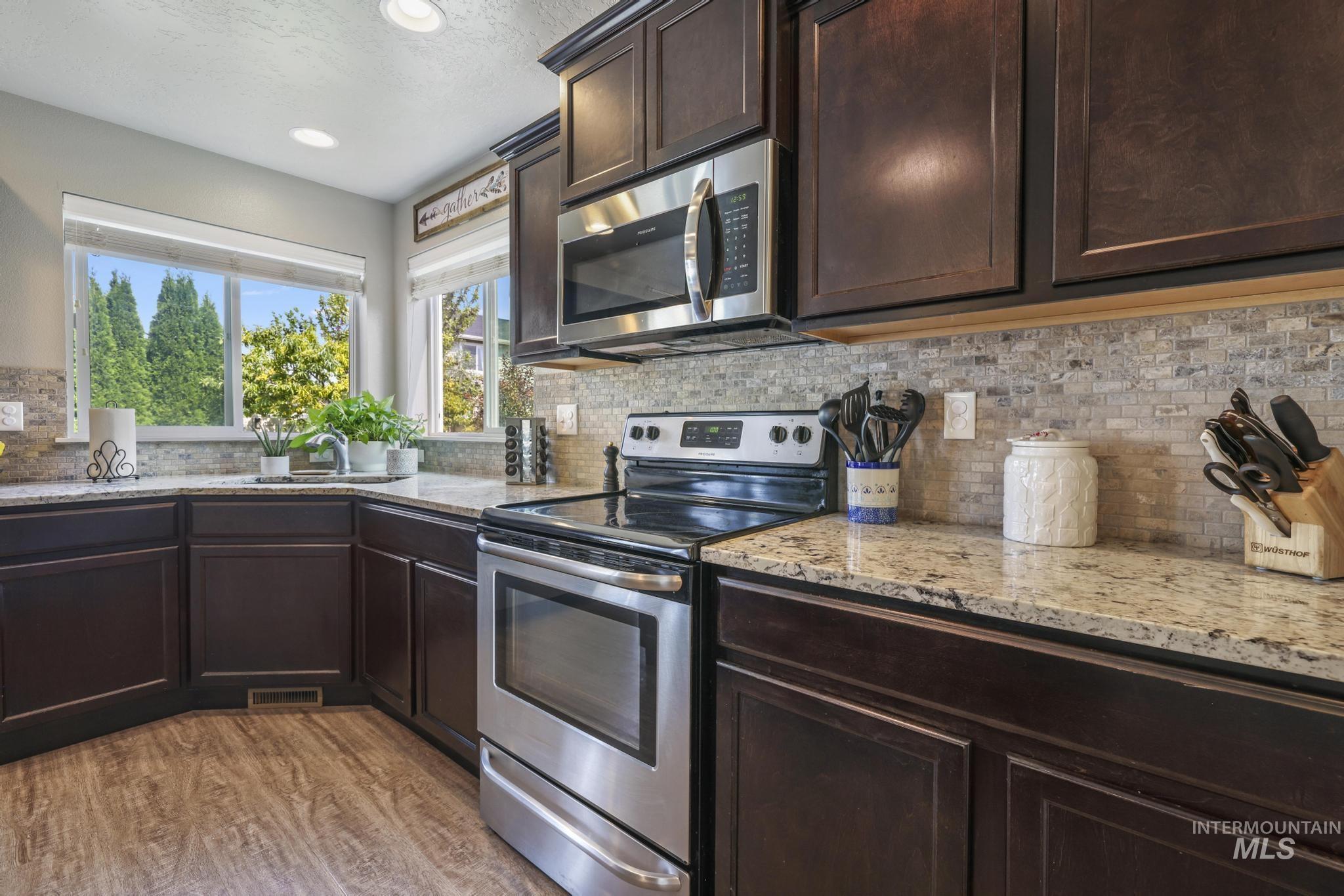 Kitchen with dark brown cabinetry, stainless steel appliances, light stone countertops, backsplash, and a textured ceiling