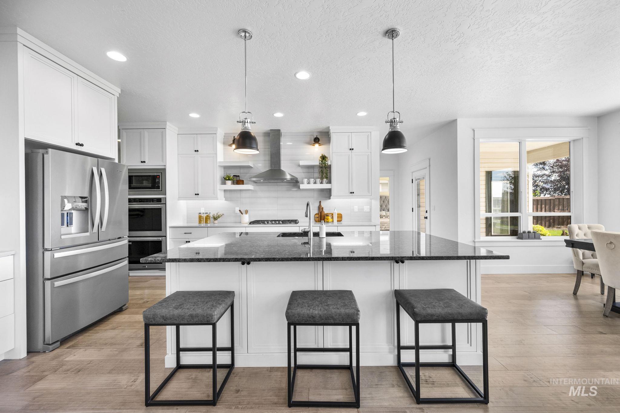 Kitchen featuring dark stone counters, appliances with stainless steel finishes, hanging light fixtures, a center island with sink, and white cabinets