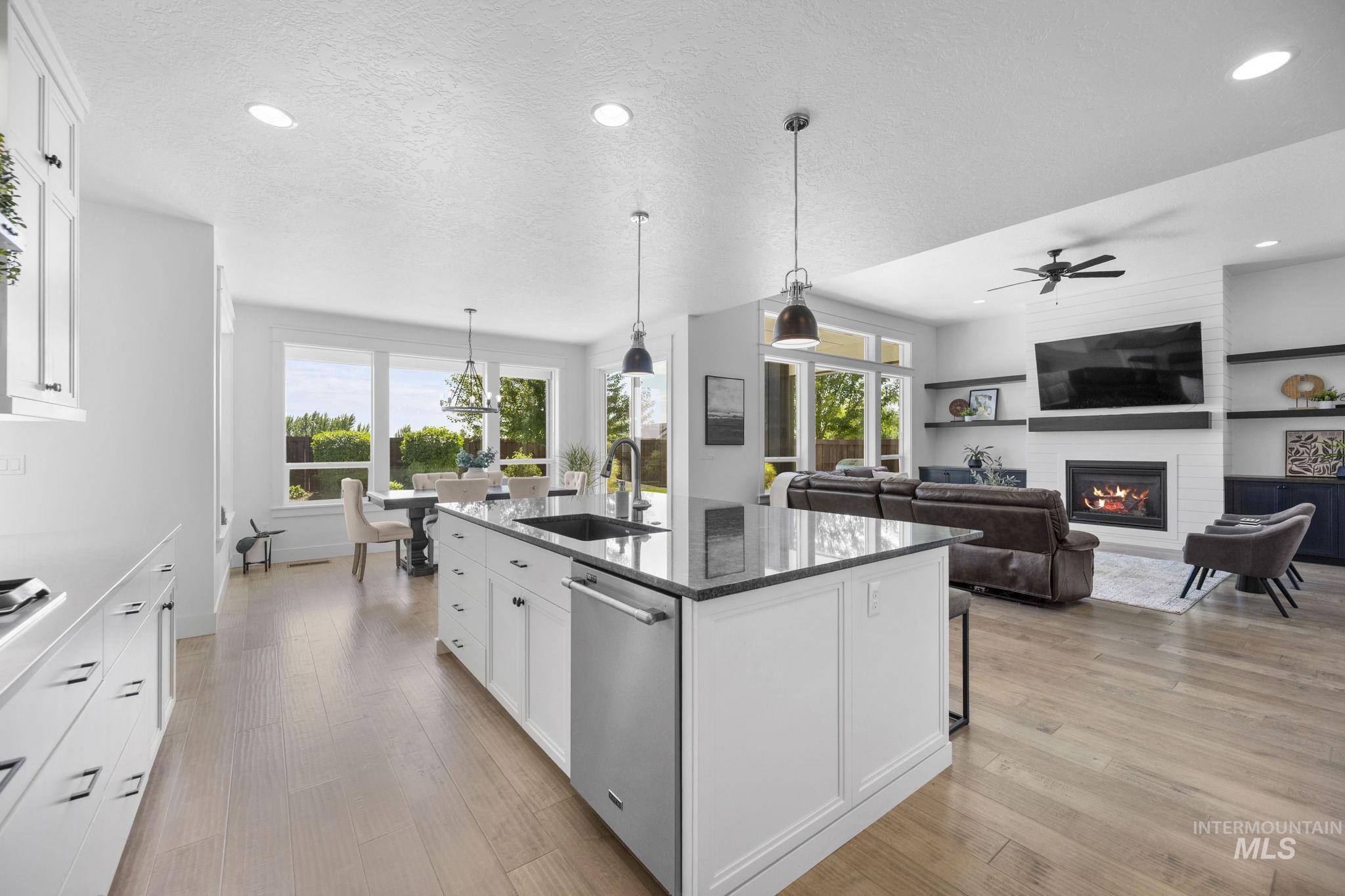 Kitchen with white cabinetry, dark stone counters, a kitchen island with sink, hanging light fixtures, and stainless steel dishwasher