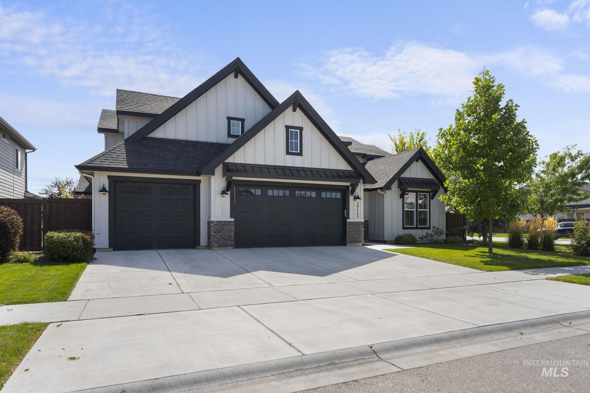 View of front facade with board and batten siding, roof with shingles, driveway, and 3 car garage.