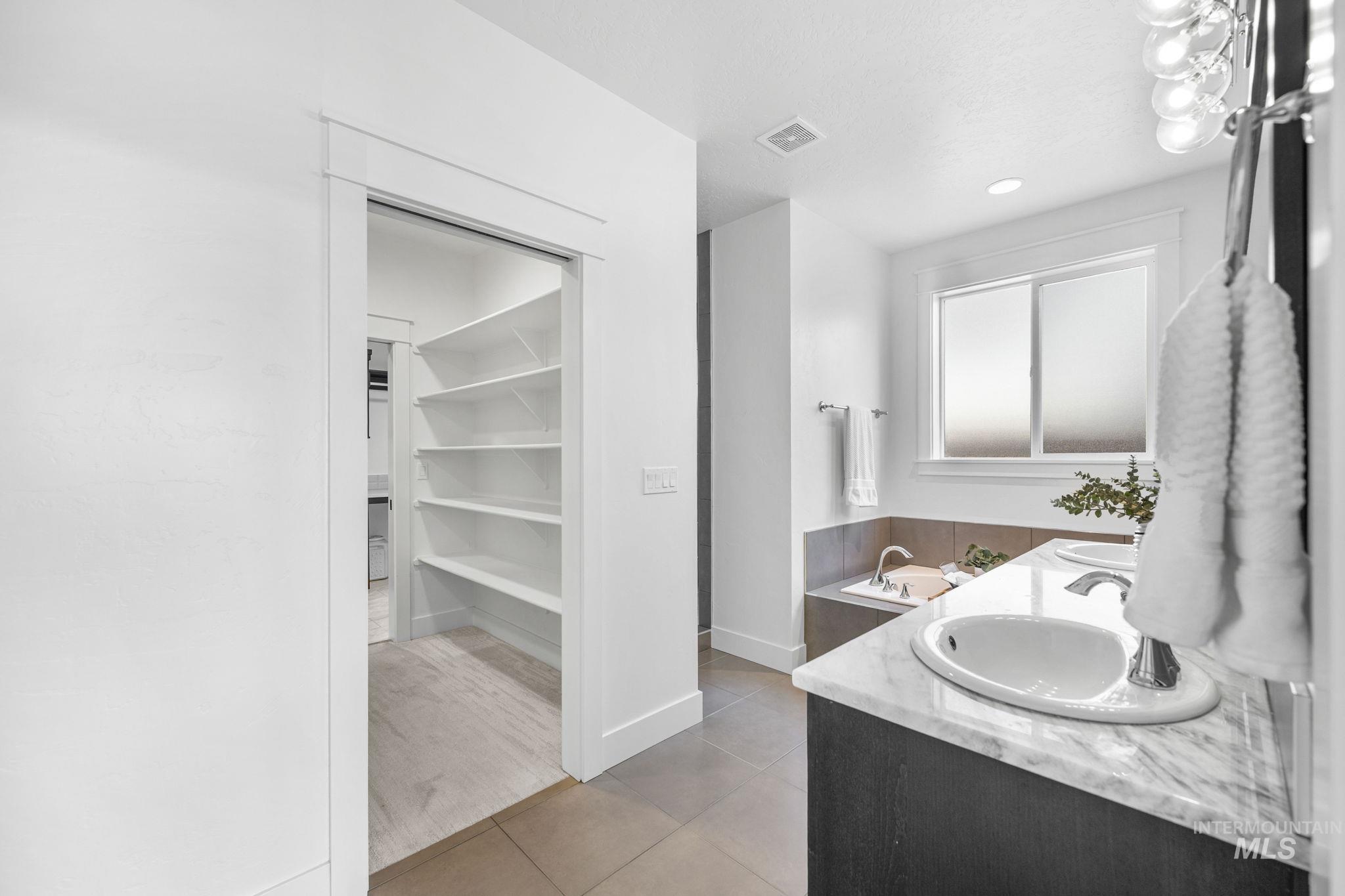 Full primary bathroom featuring light tile patterned floors, double vanity, a spacious closet, and recessed lighting