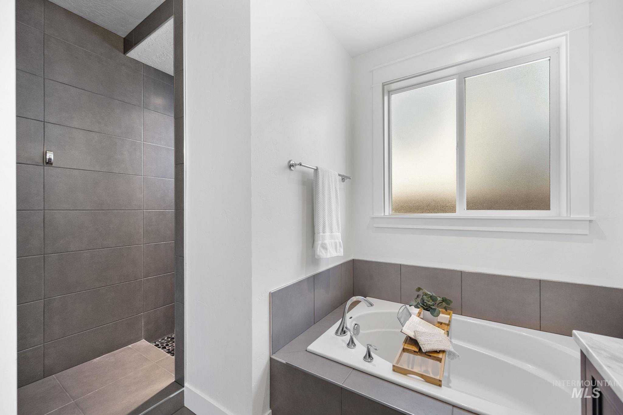 Full primary bathroom featuring a soaker tub, vanity, and a tile shower