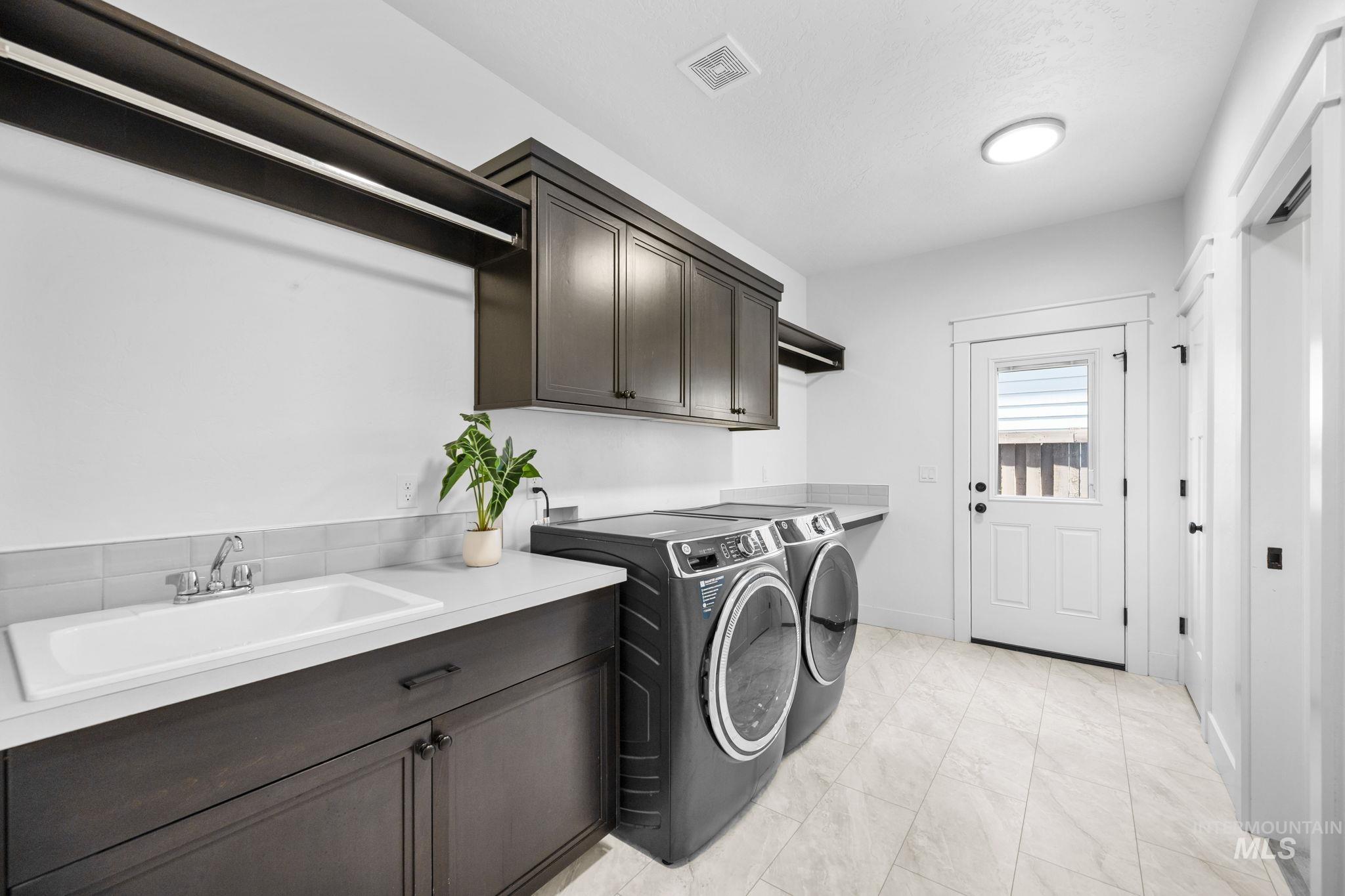 Spacious laundry room featuring independent washer and dryer, additional cabinet space, and side door access to East side exterior of the home.