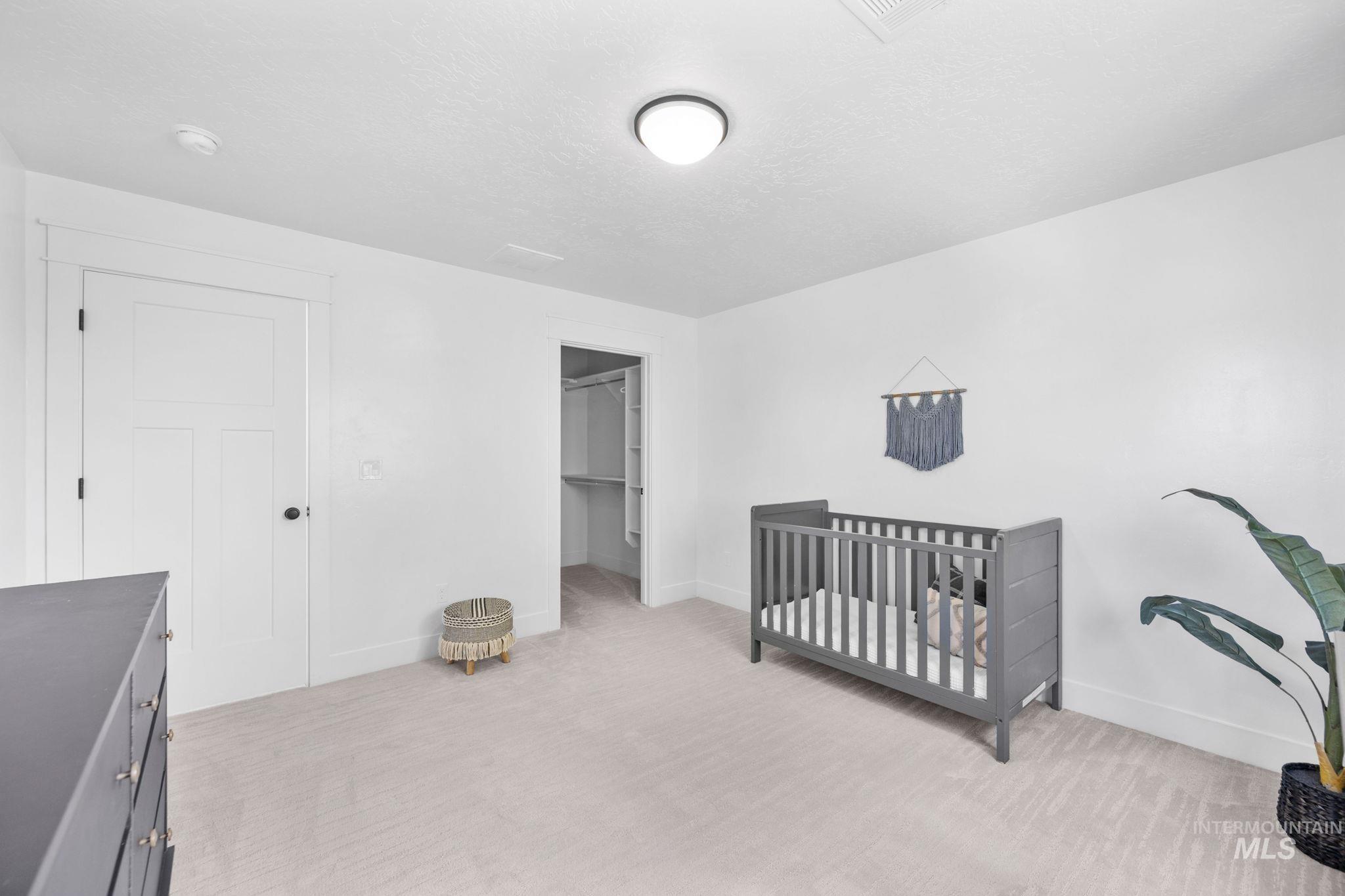 Second story bedroom with light carpet, a spacious closet, a crib, and a textured ceiling