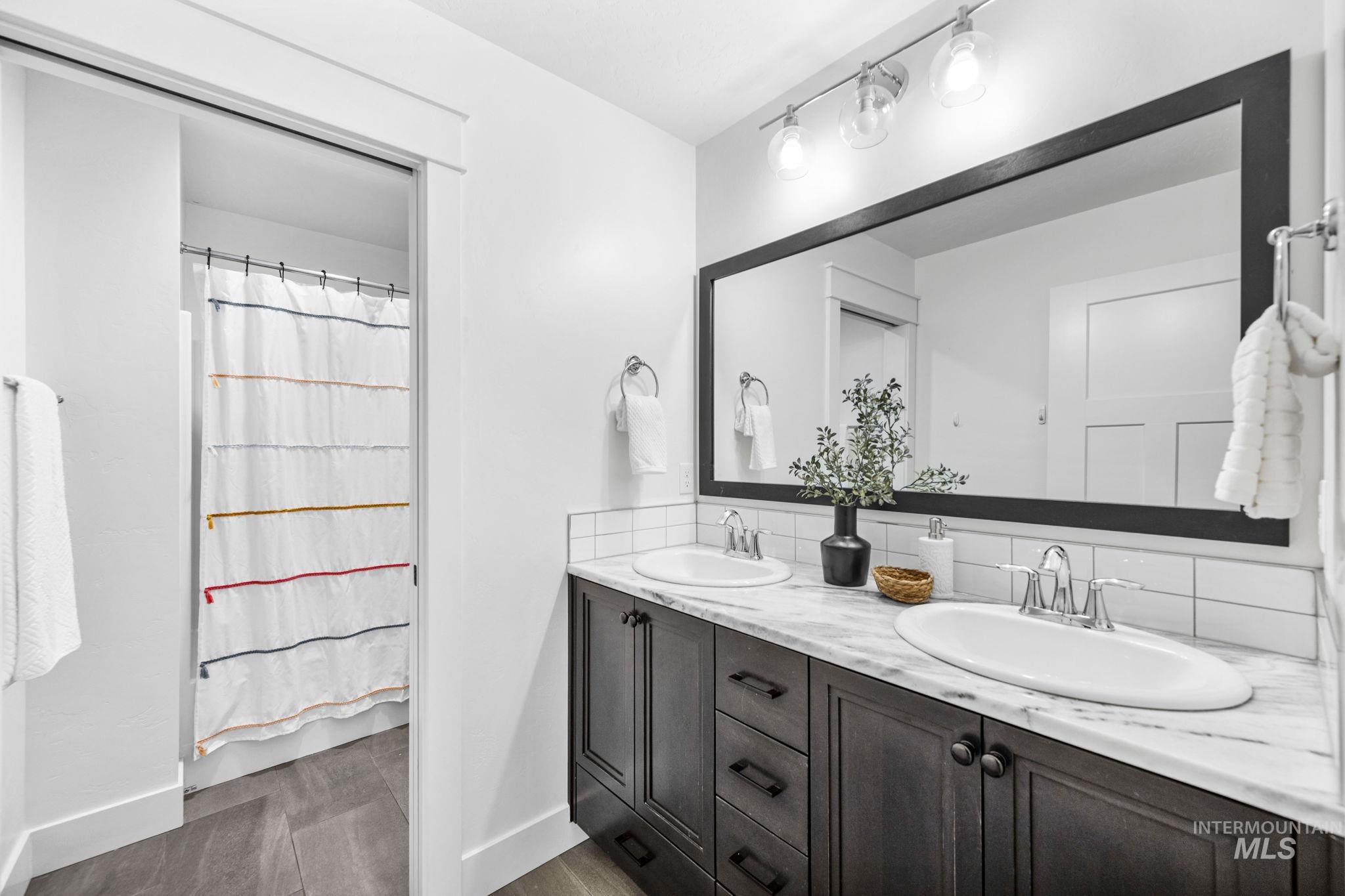 Second story full bathroom with double vanity, decorative backsplash, dark wood-style flooring, and a shower with shower curtain