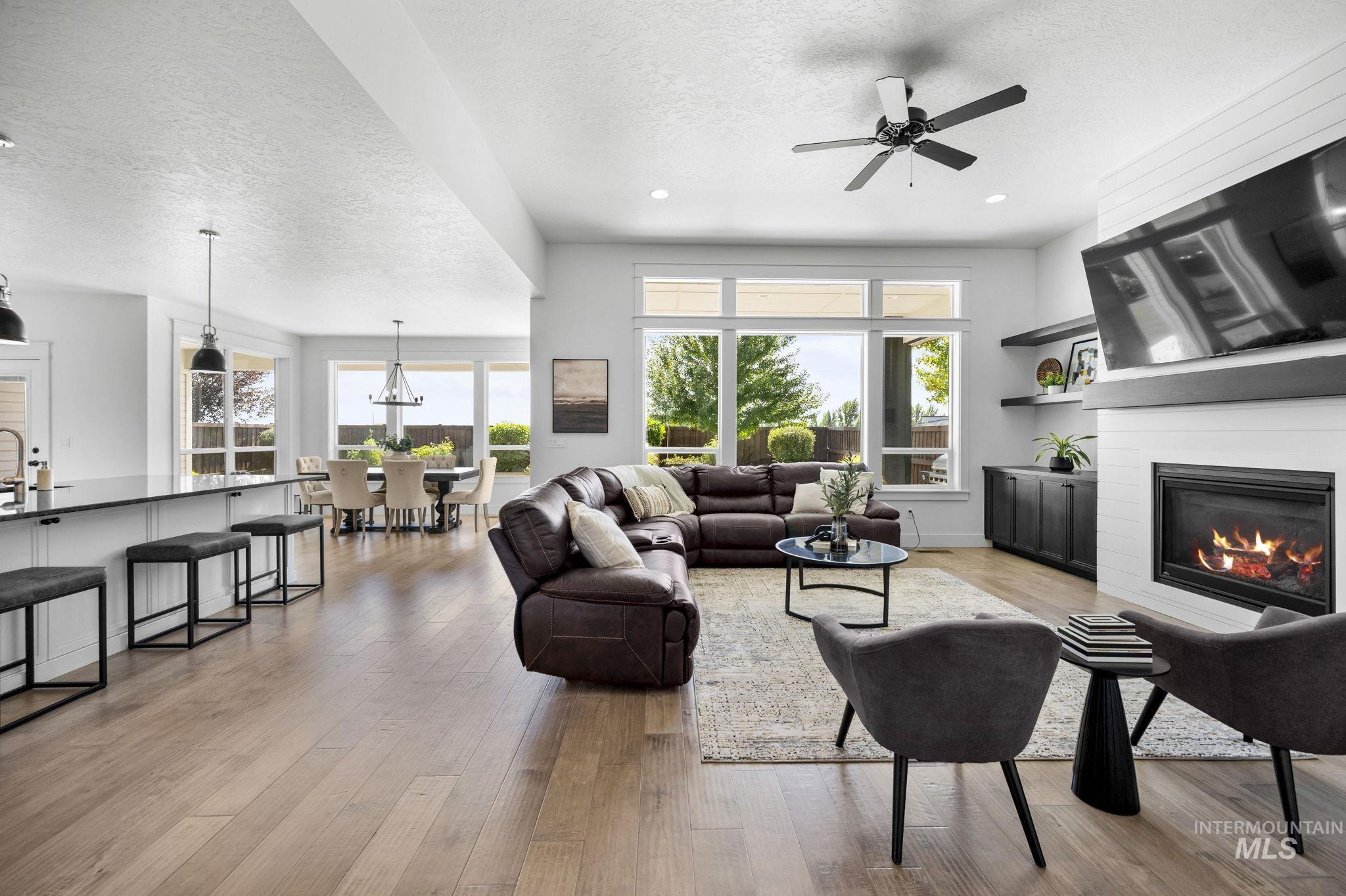 Living area with a textured ceiling, light wood-style flooring, a glass covered fireplace, ceiling fan, and recessed lighting
