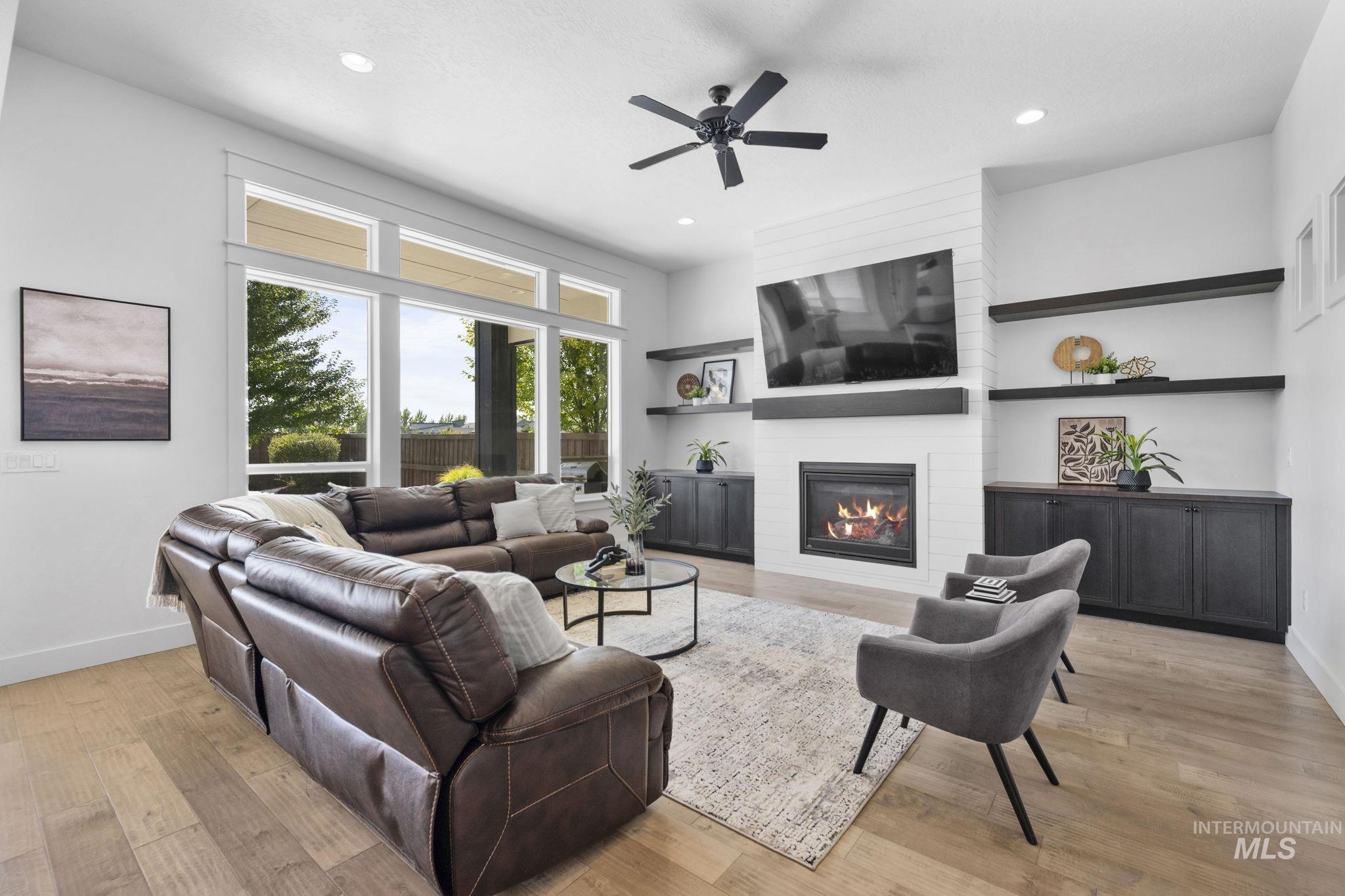Living area with a large fireplace, light wood-style flooring, a ceiling fan, and recessed lighting