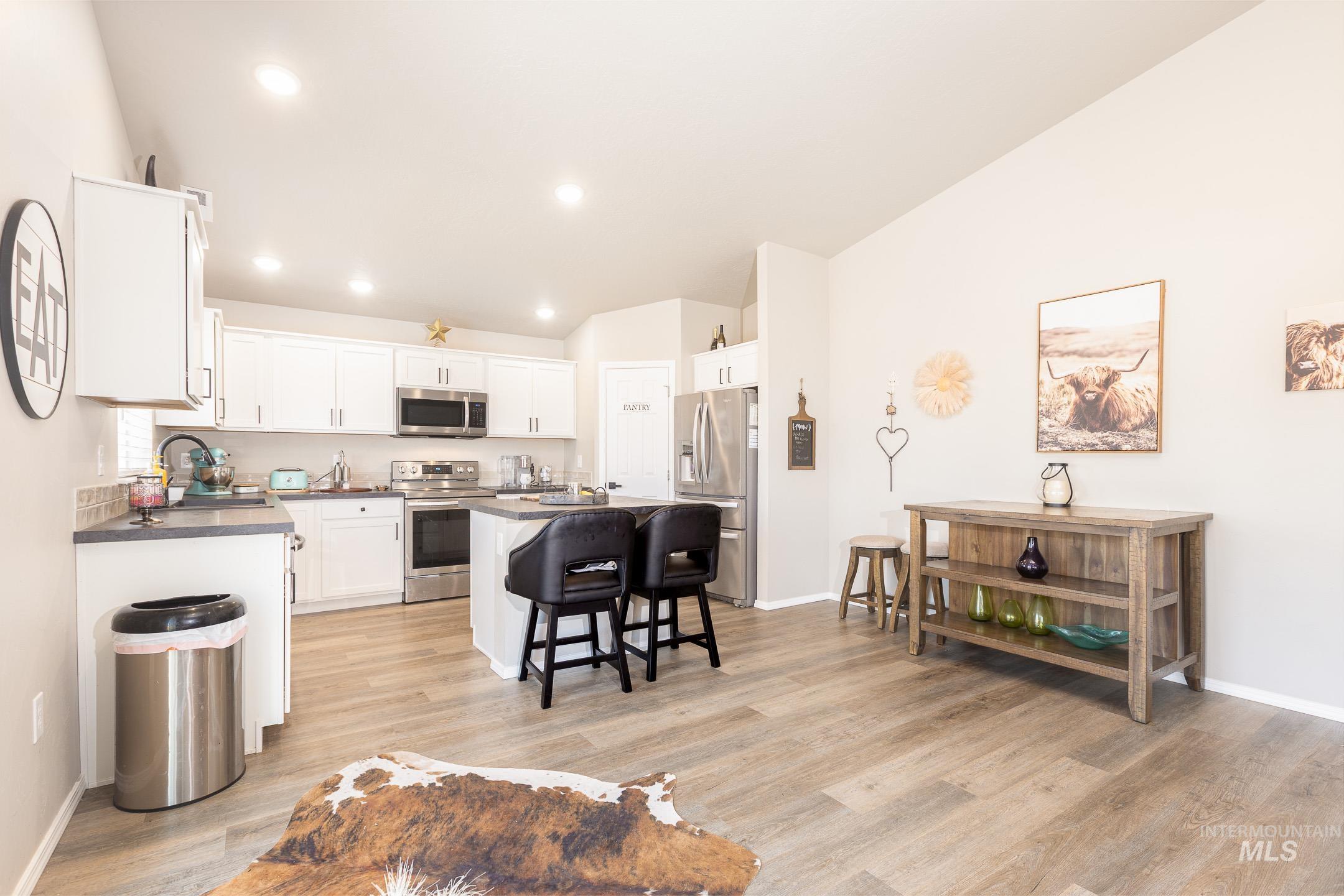 Kitchen with a kitchen bar, stainless steel appliances, dark countertops, white cabinets, and a center island