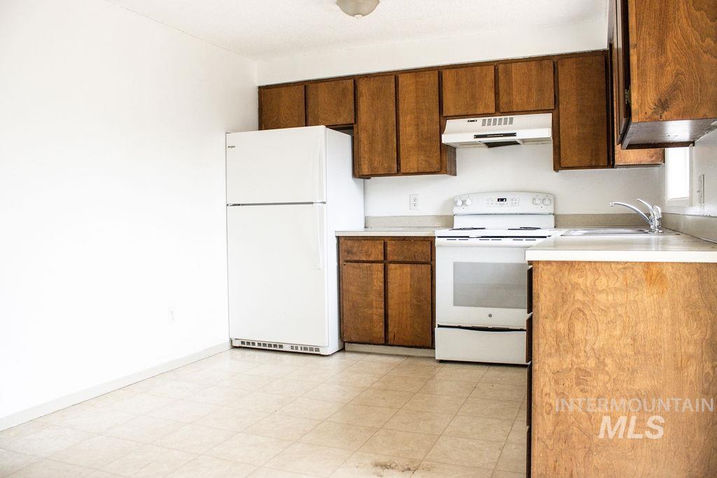 Kitchen with white appliances, light countertops, under cabinet range hood, light floors, and brown cabinetry