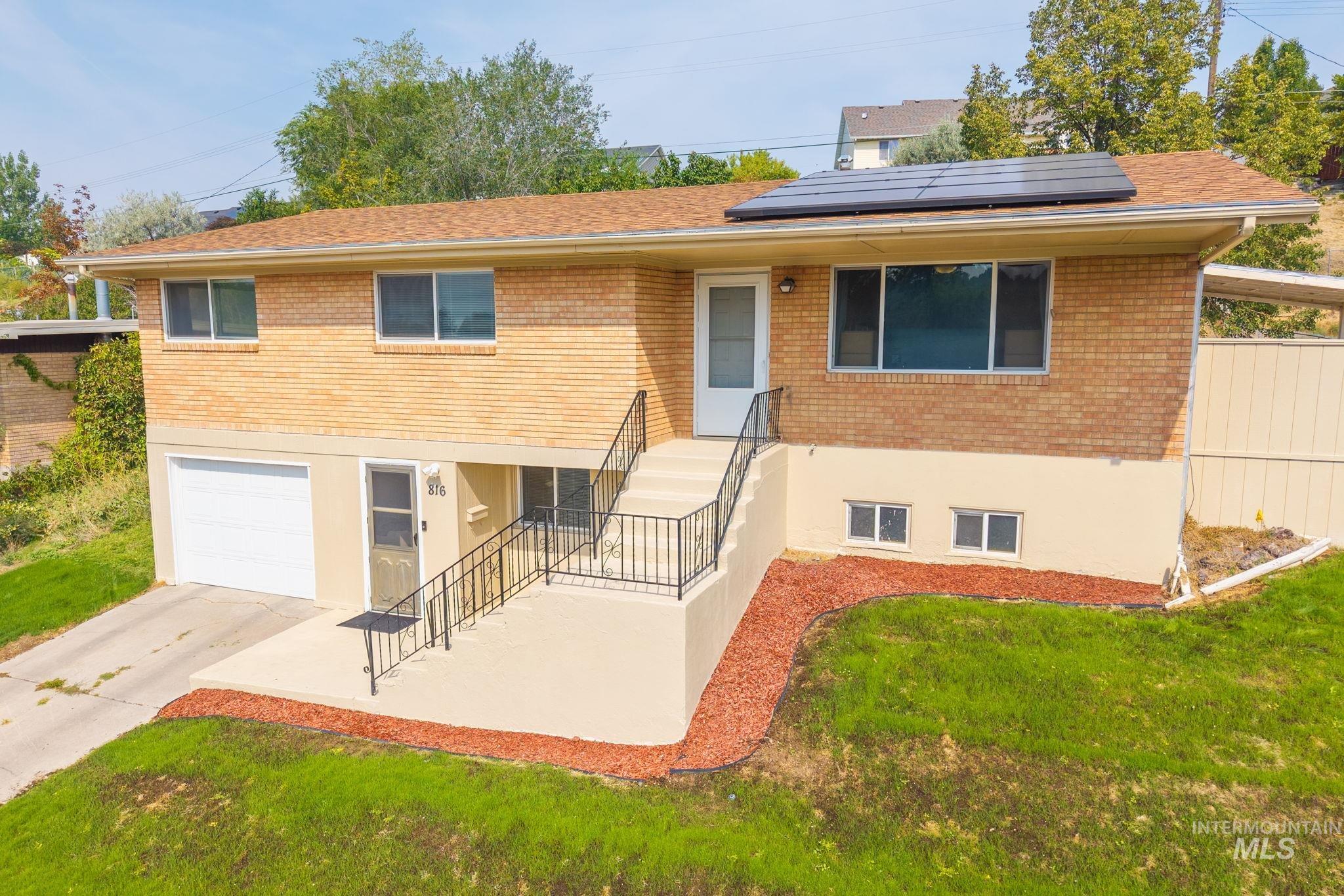 View of front facade featuring brick siding, roof mounted solar panels, an attached garage, and driveway