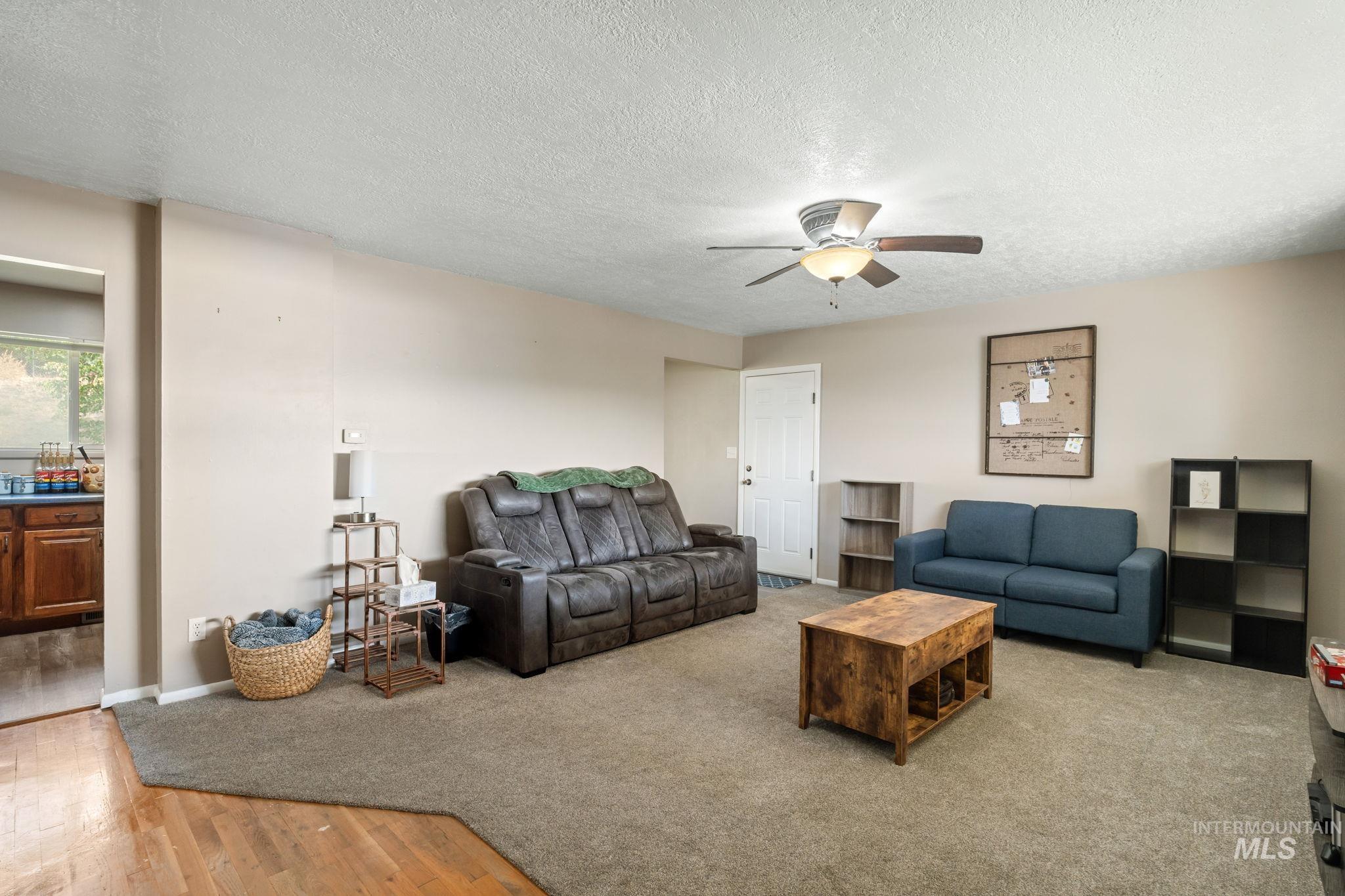 Living room with a textured ceiling, light wood-style flooring, ceiling fan, and light colored carpet
