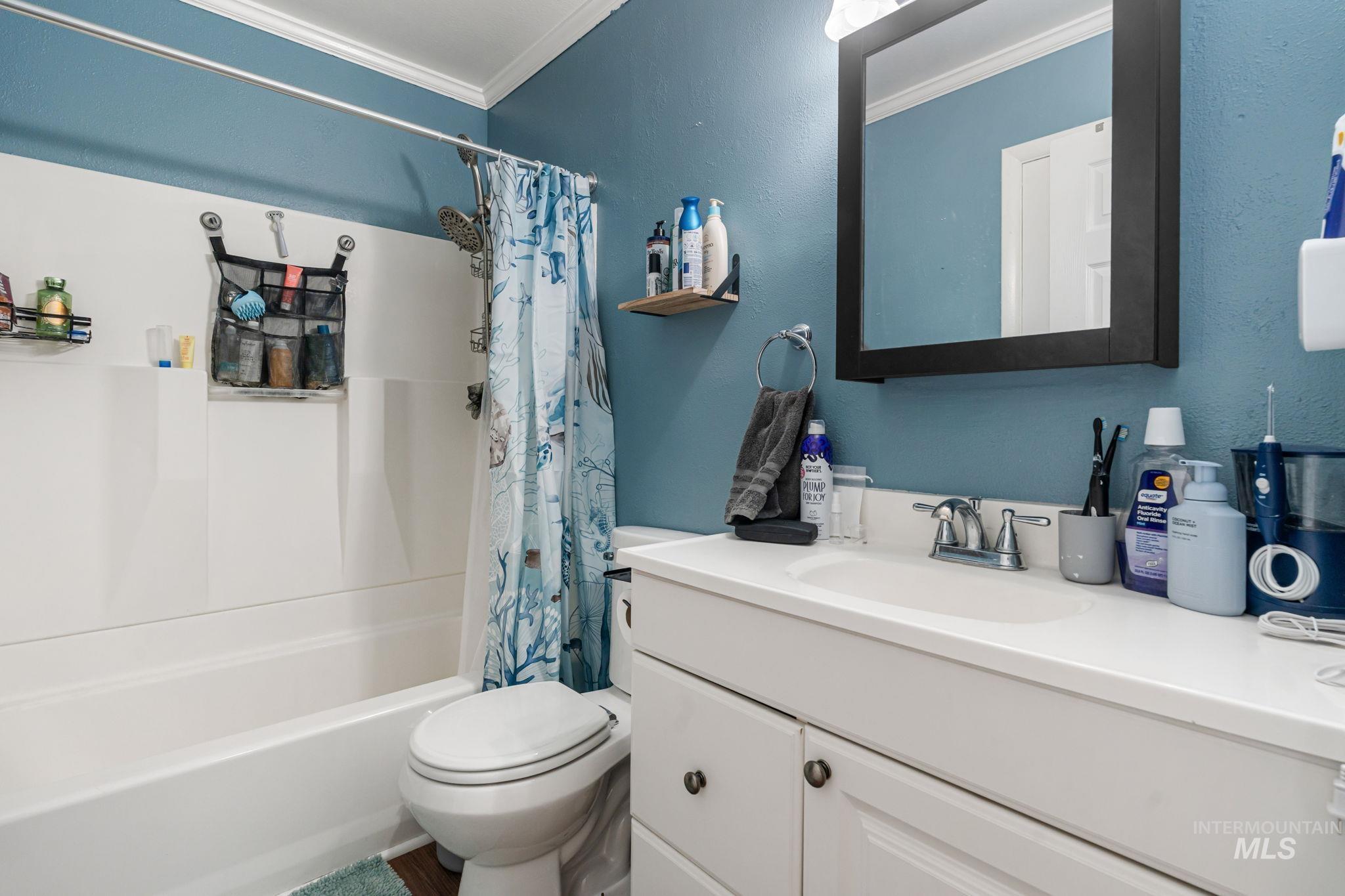 Full bathroom with shower / tub combo with curtain, vanity, ornamental molding, and a textured wall