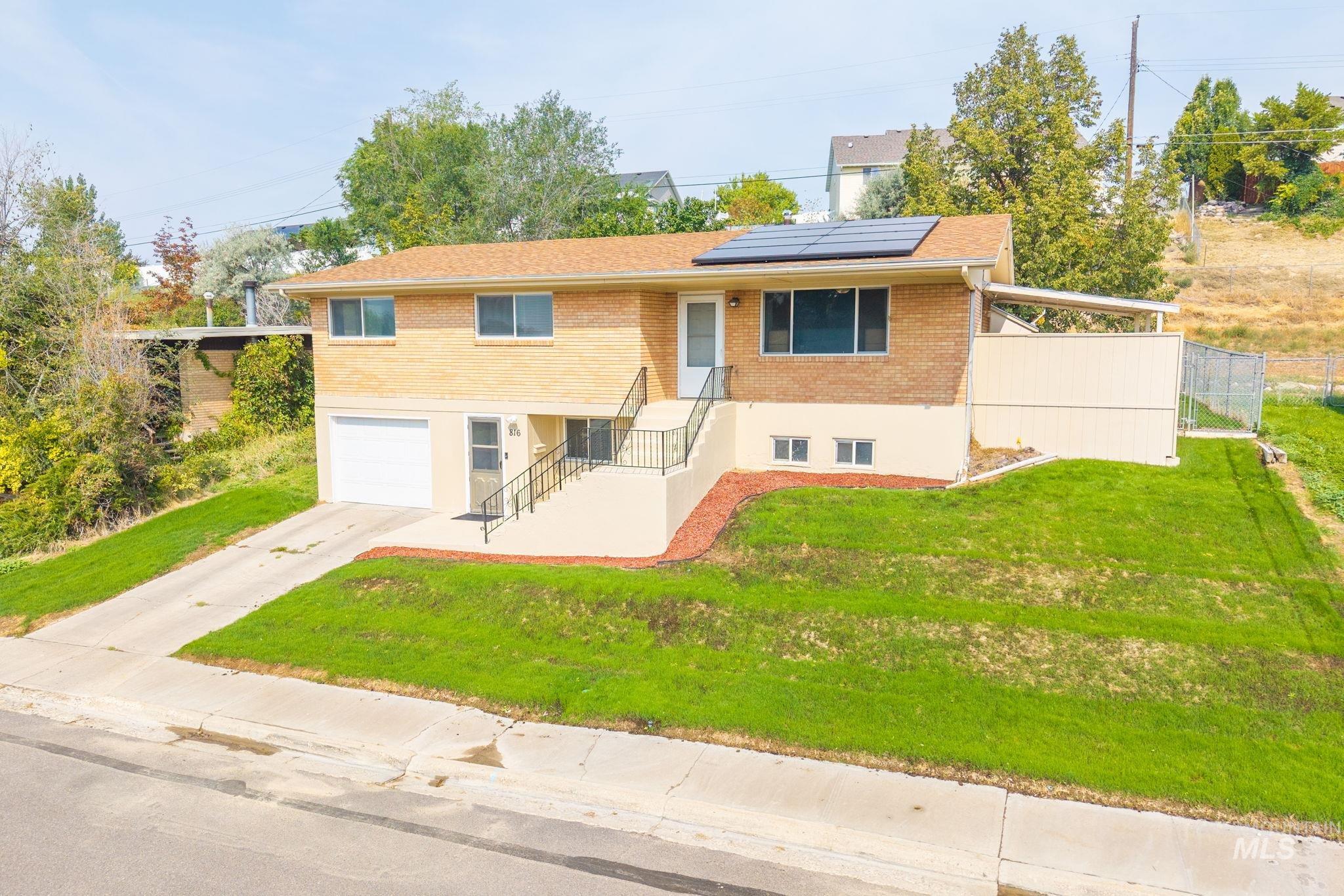 View of front facade featuring brick siding, roof mounted solar panels, concrete driveway, and an attached garage