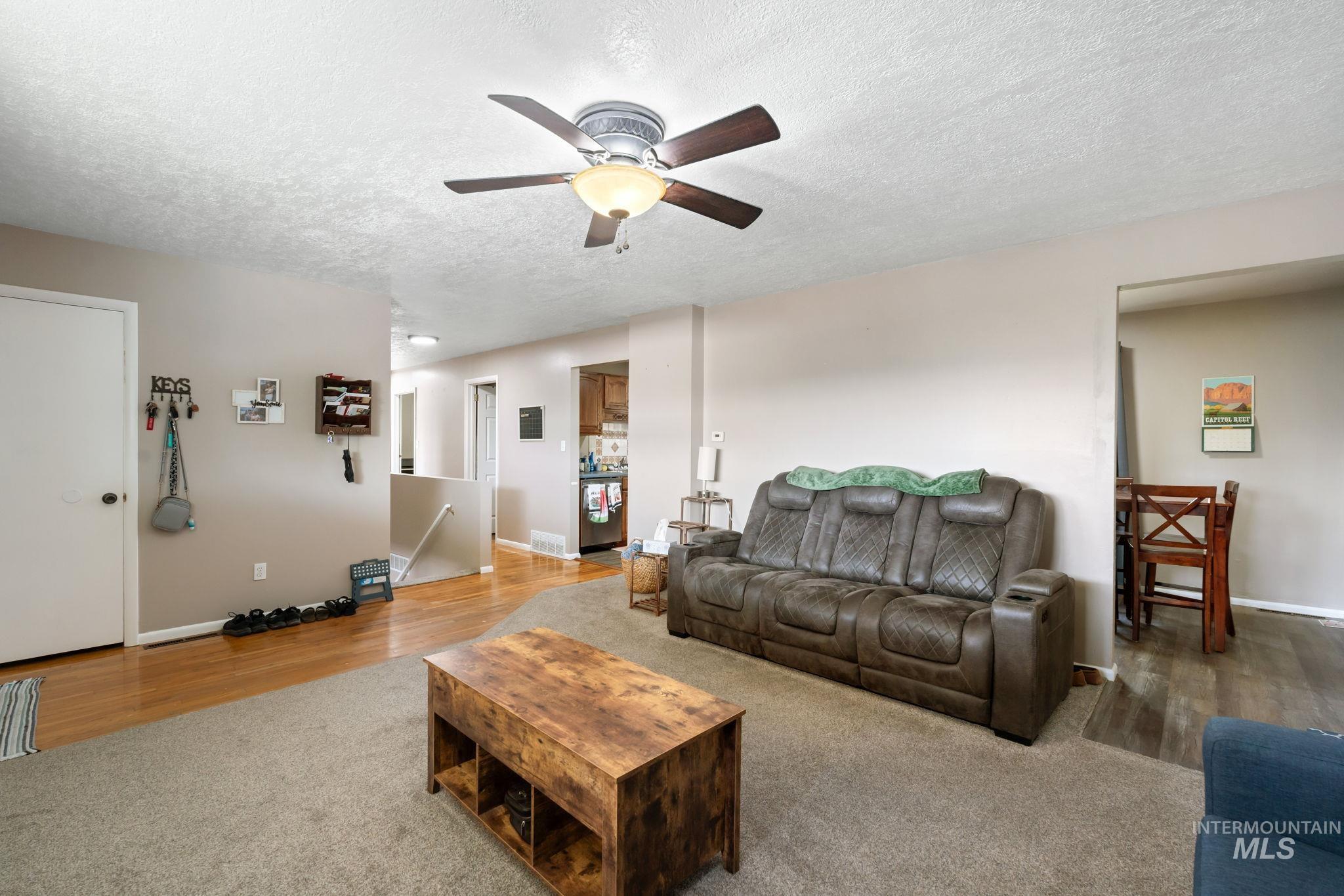 Carpeted living area featuring a textured ceiling, wood finished floors, and ceiling fan