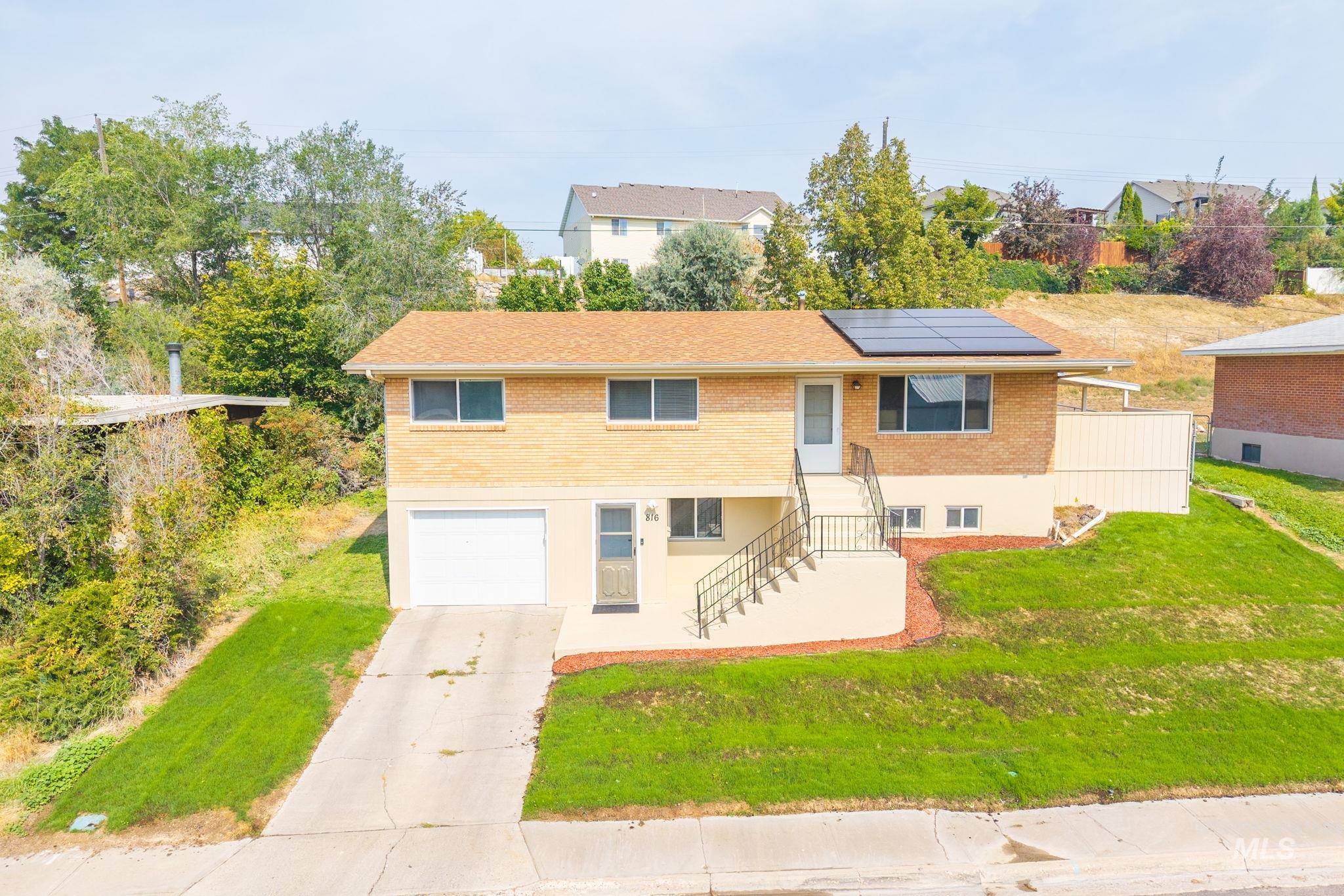 View of front of house with brick siding, solar panels, driveway, a front yard, and an attached garage