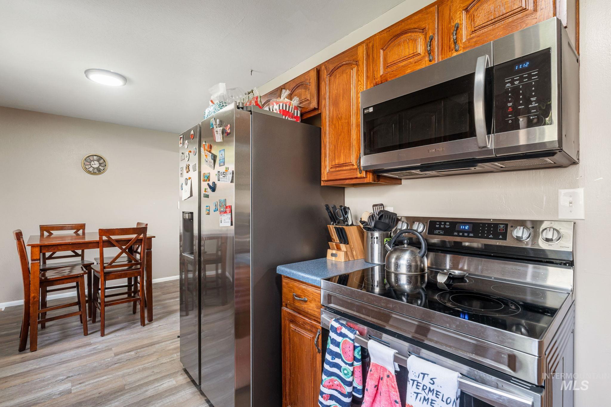 Kitchen featuring appliances with stainless steel finishes, brown cabinets, light wood-type flooring, and dark countertops