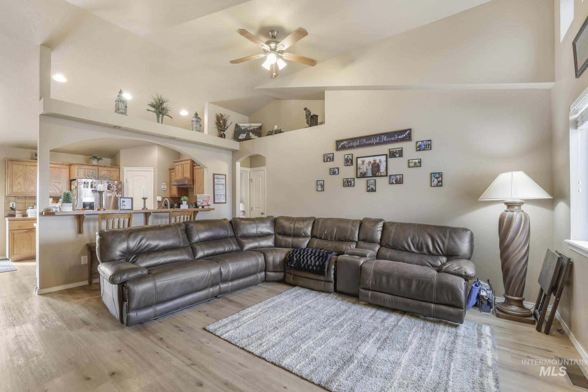 Living room featuring arched walkways, high vaulted ceiling, light wood-type flooring, and a ceiling fan