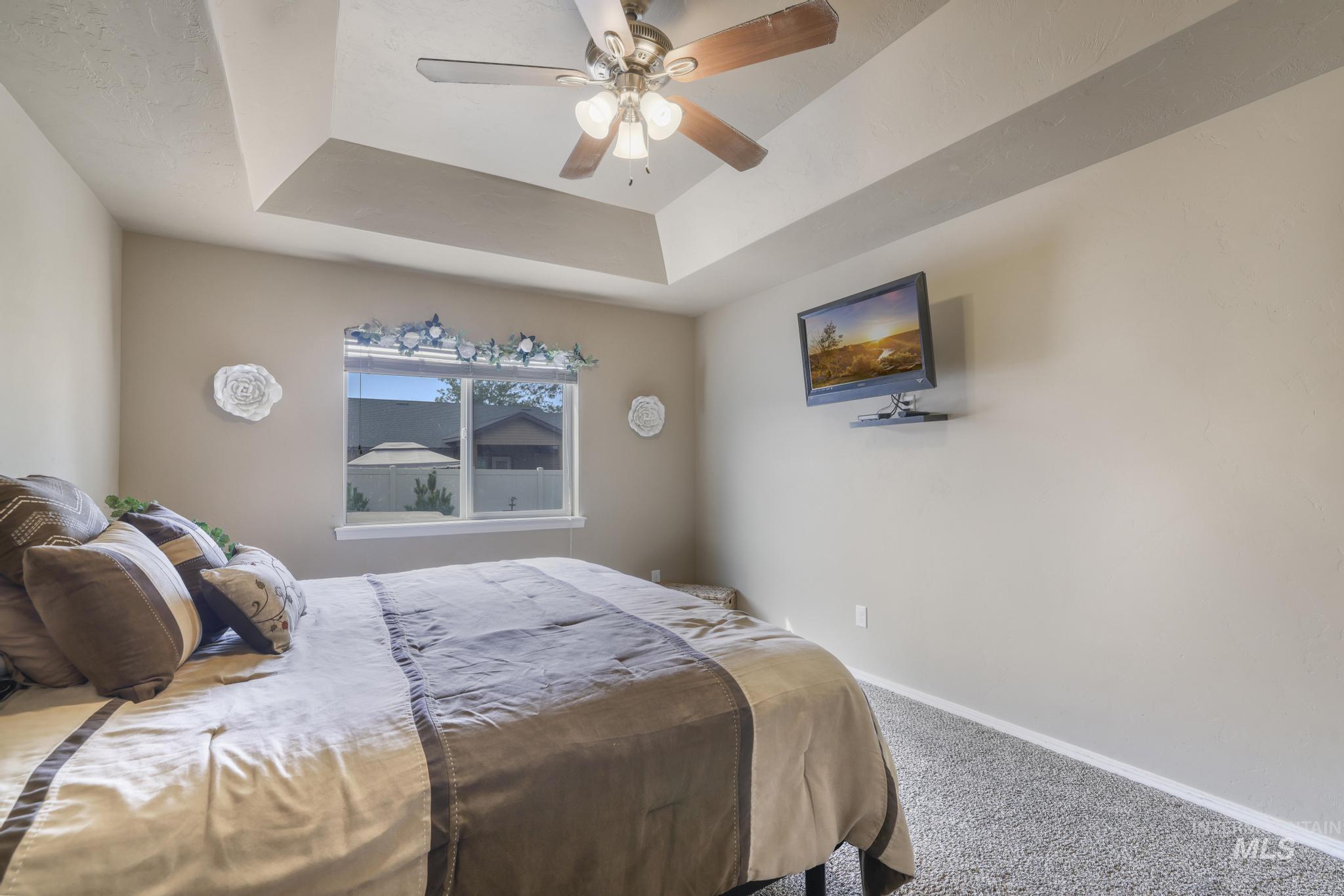 Bedroom featuring a raised ceiling, carpet, and ceiling fan
