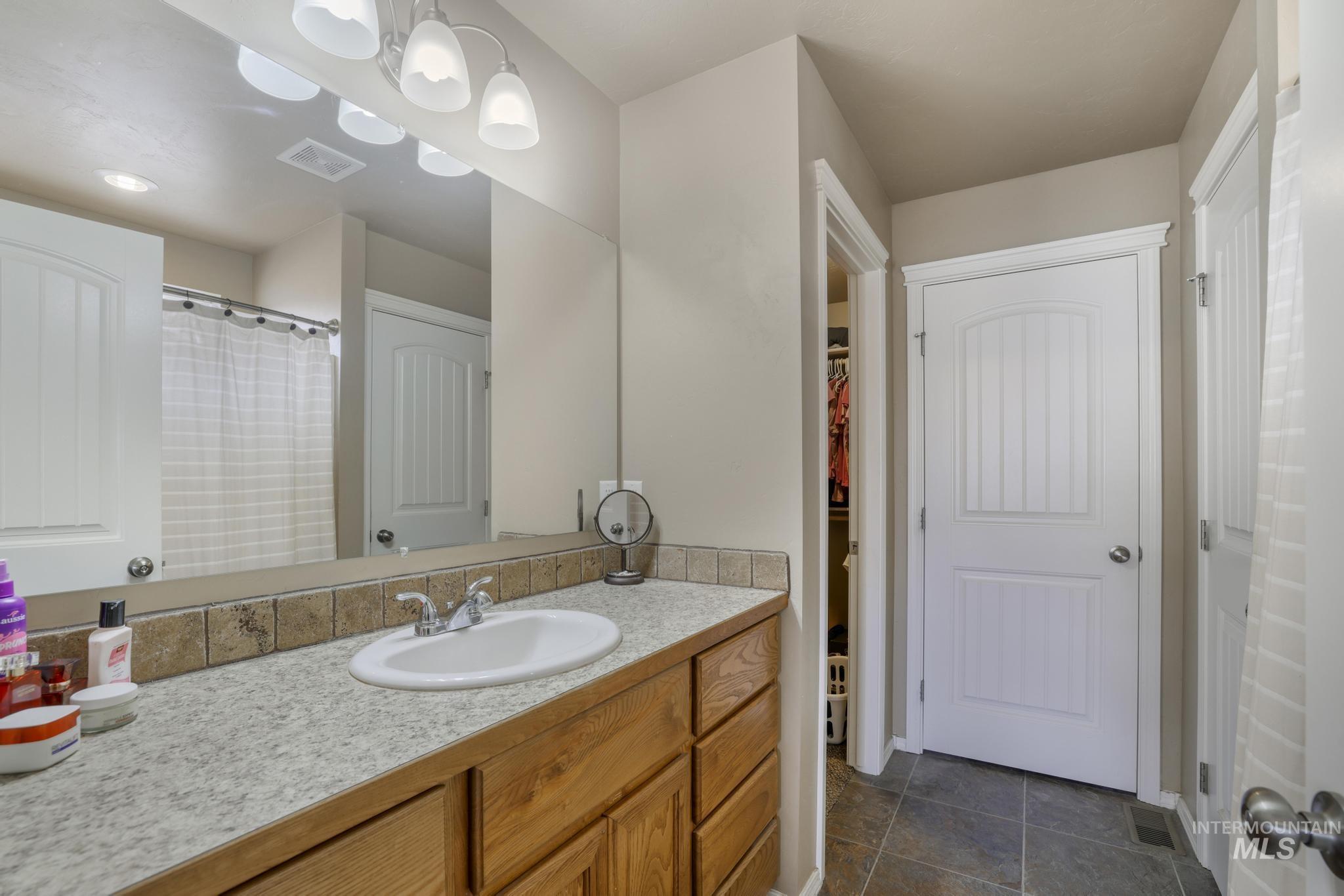 Bathroom featuring vanity, a spacious closet, dark tile patterned floors, and a shower with curtain